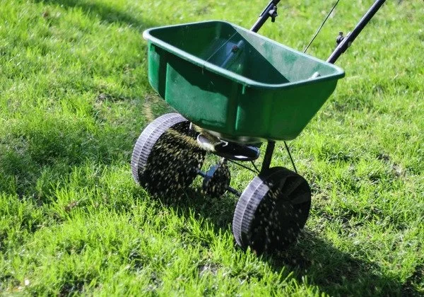 broadcast spreader rolling over lawn spreading fertilizer