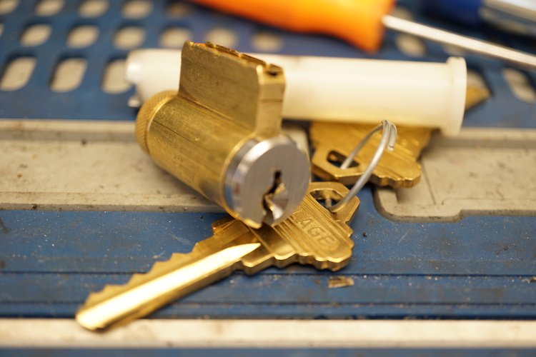 lock cylinder atop two house keys with rekeying tools in background