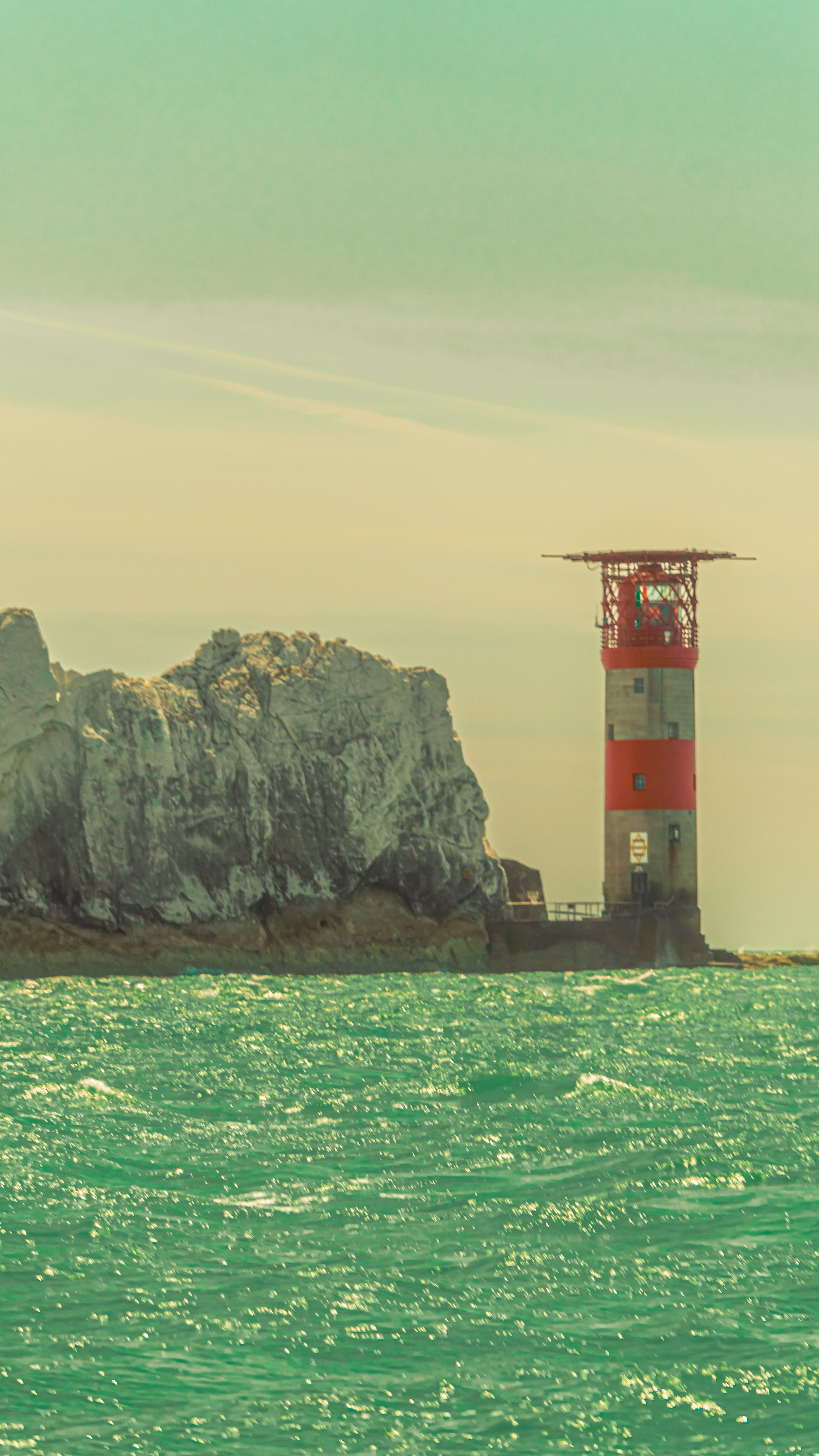 A lighthouse on a rocky coastline beside the water, with an overcast sky.