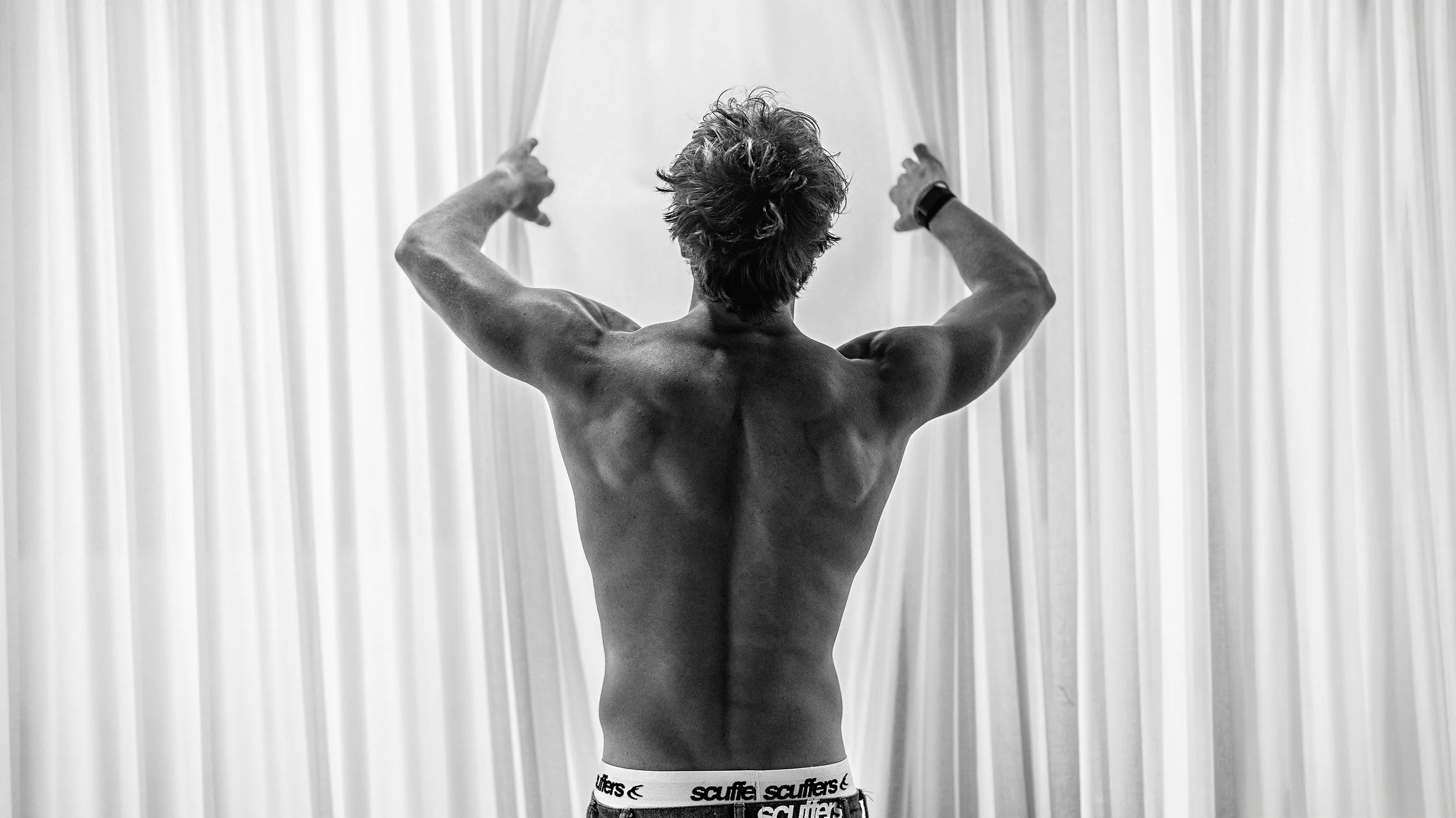 Influencer Keenan Chapman standing in front of a window, showing off his muscles.