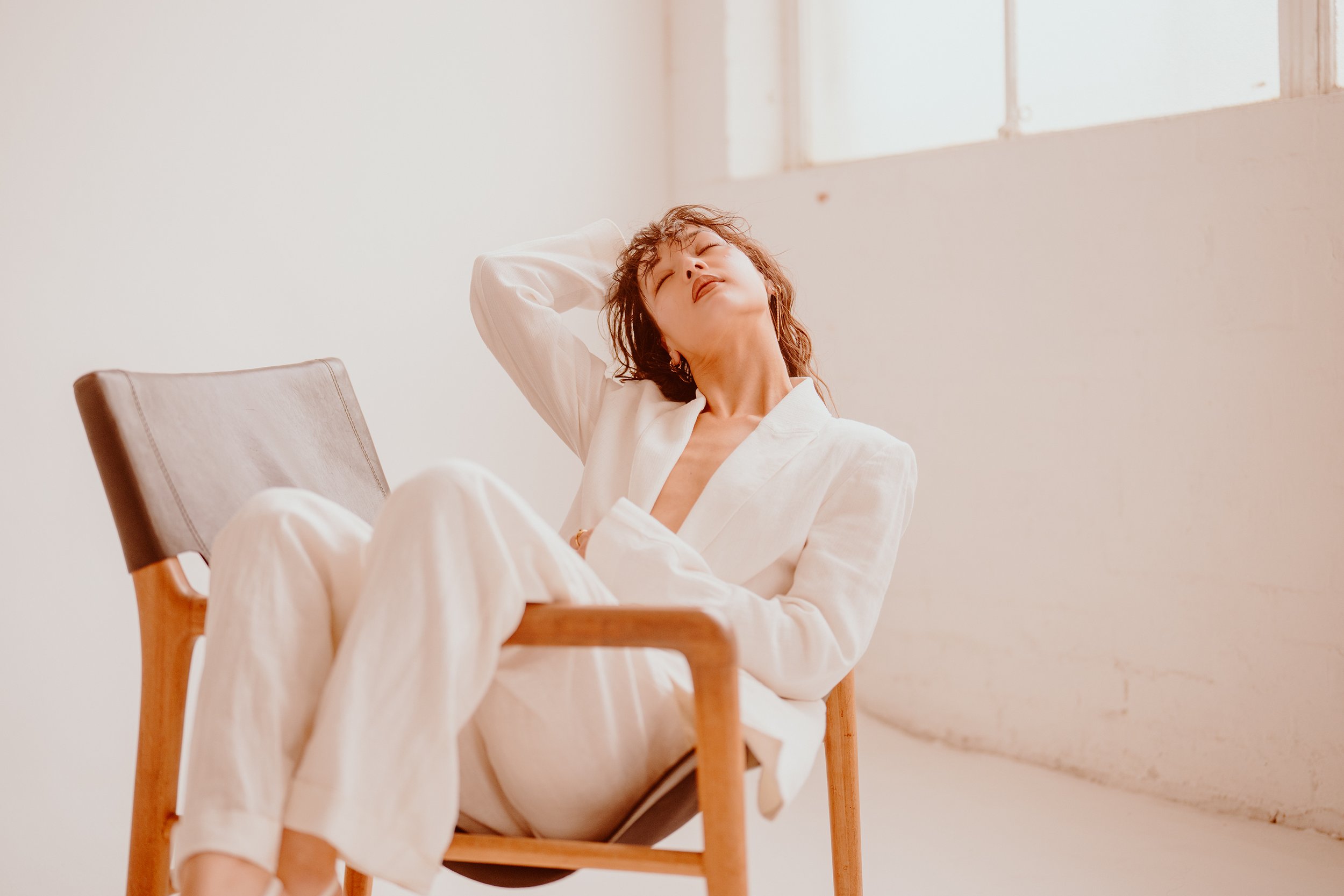 Melbourne model Soph Xu, wearing white suit, plenty of attitude, laying back and draped over a chair, captured by photographer Campbell Mattinson.