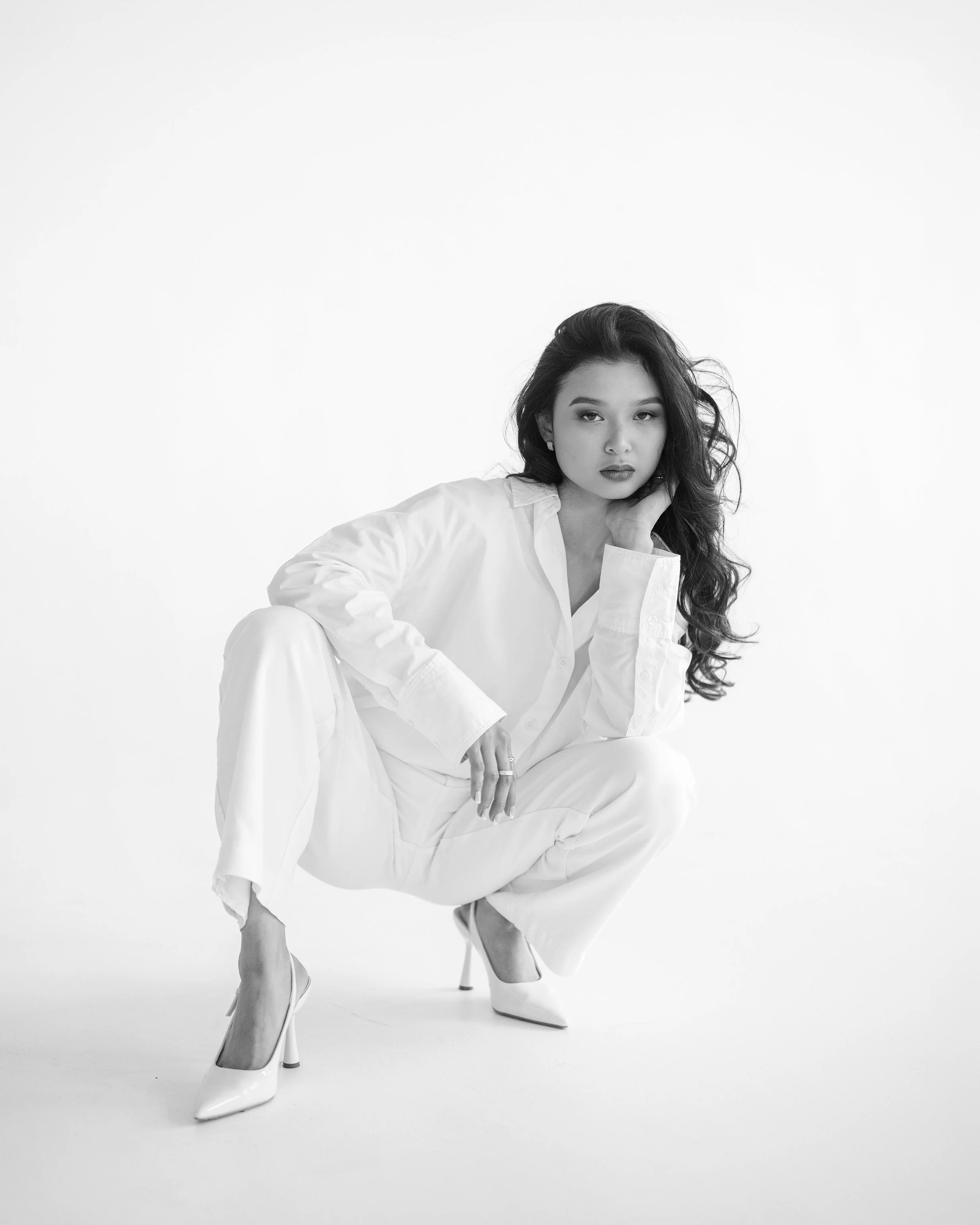 Melbourne model Veronica Ty, wearing a white suit, against a white background, crouches down and looks straight at the camera.
