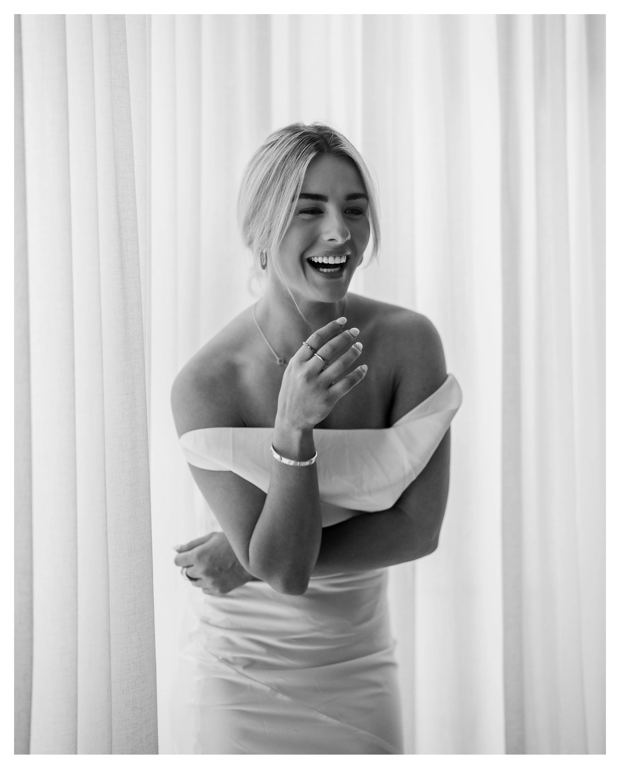 Image of Shanelle Hodgkinson in a white wedding dress, laughing in front of white curtains.