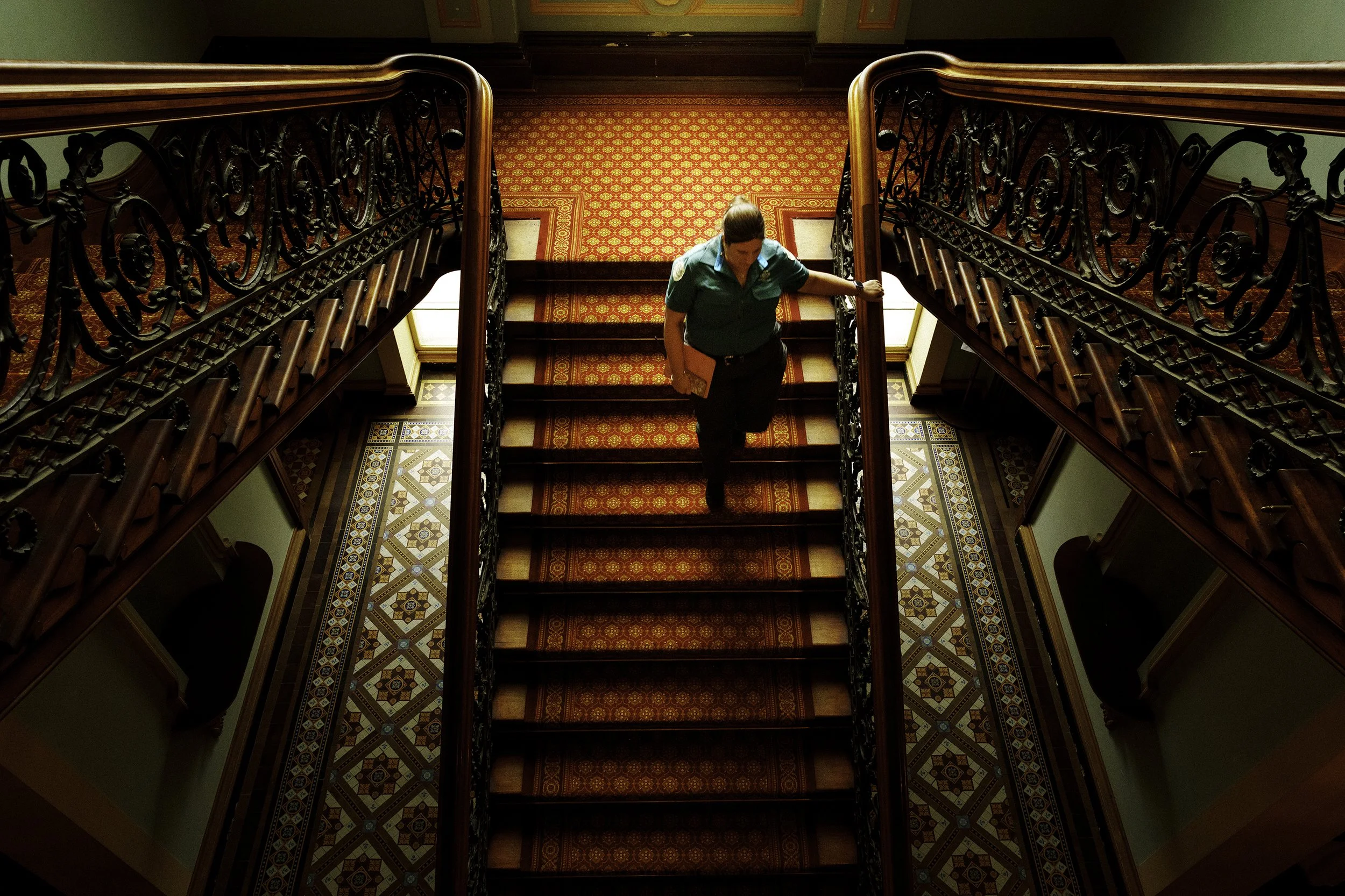 A Parks Victoria staffer on the grand staircase in the entrance foyer of the Werribee Park Mansion, shot from above.
