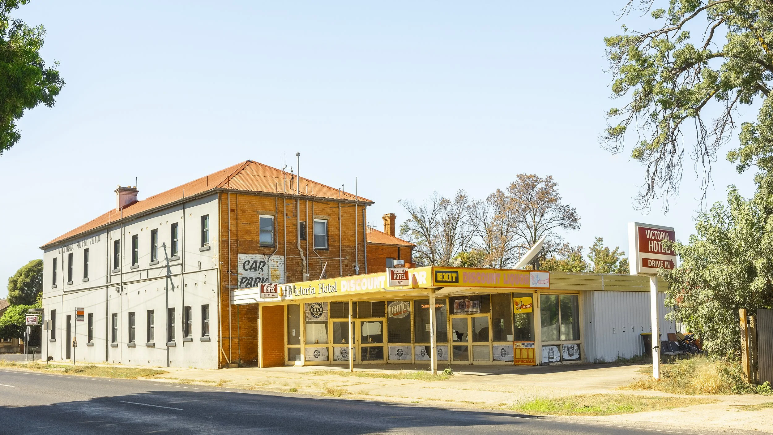 The historic Victoria Hotel in Benalla, side view, unrestored, bottle shop at the back with broken windows, hot sunny day.