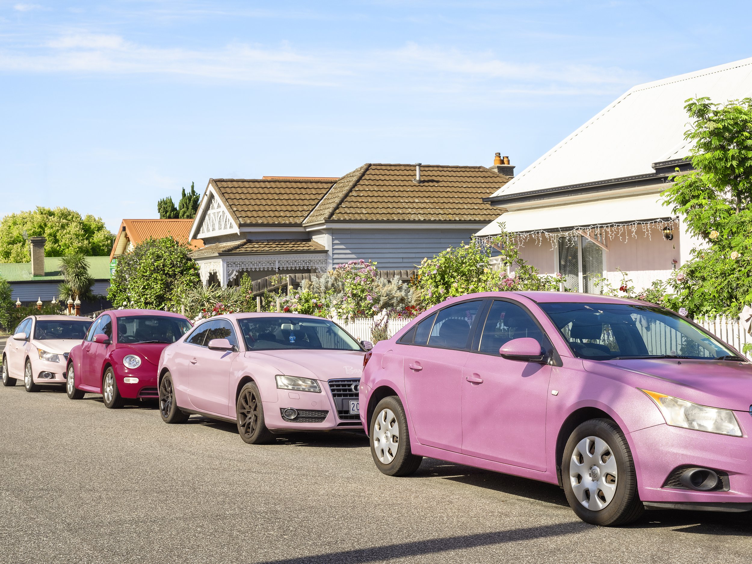 A row of four pink cars in front of a pink house in Footscray.