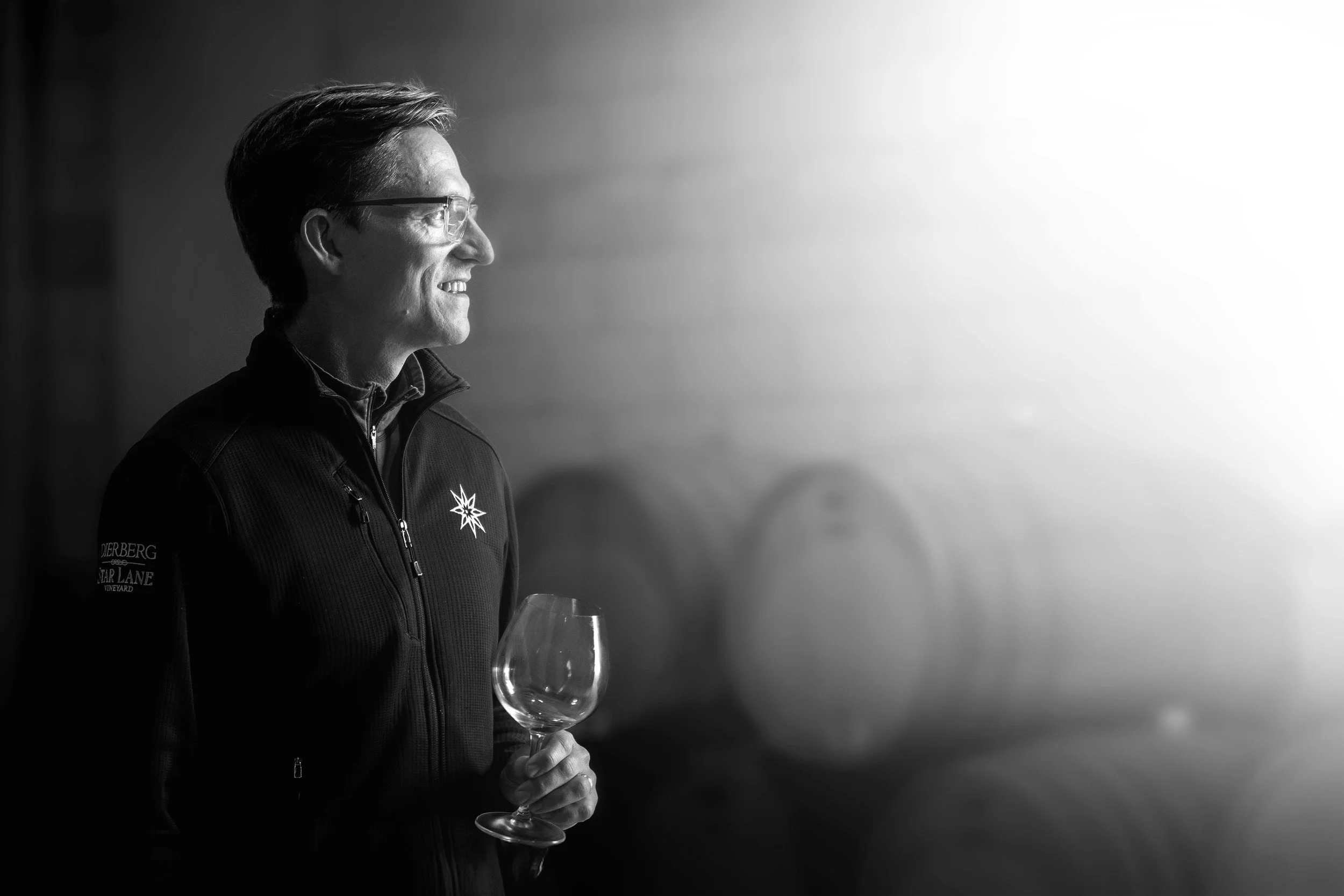 Dierberg winemaker Tyler Thomas stands, holding a wine glass, at the door of the cellar with light beaming in through the opening.