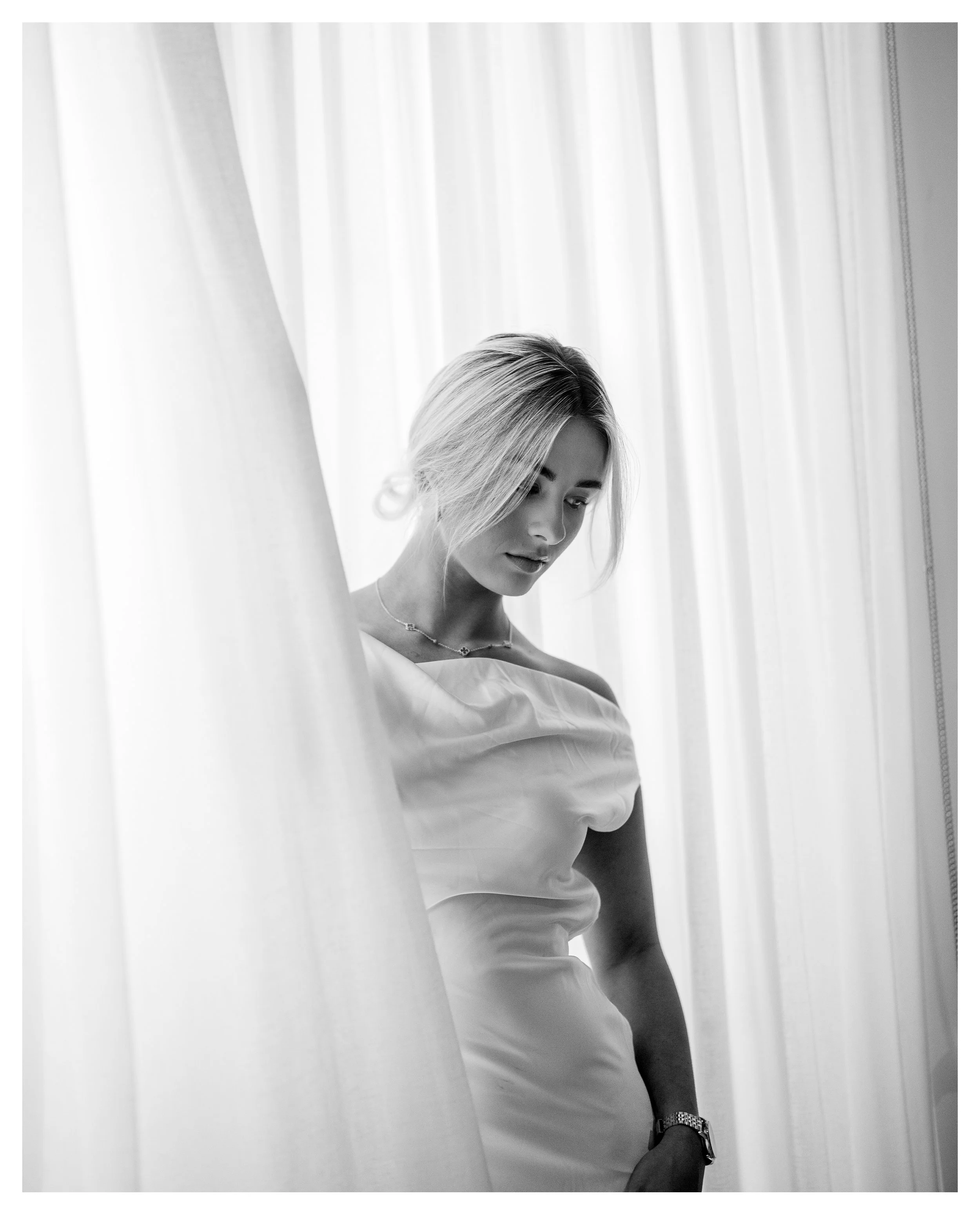 Stunning image of model Shanelle Hodgkinson in a sheer white dress, looking pensive, white sheer curtains behind her. Black and white. Photo by Campbell Mattinson.