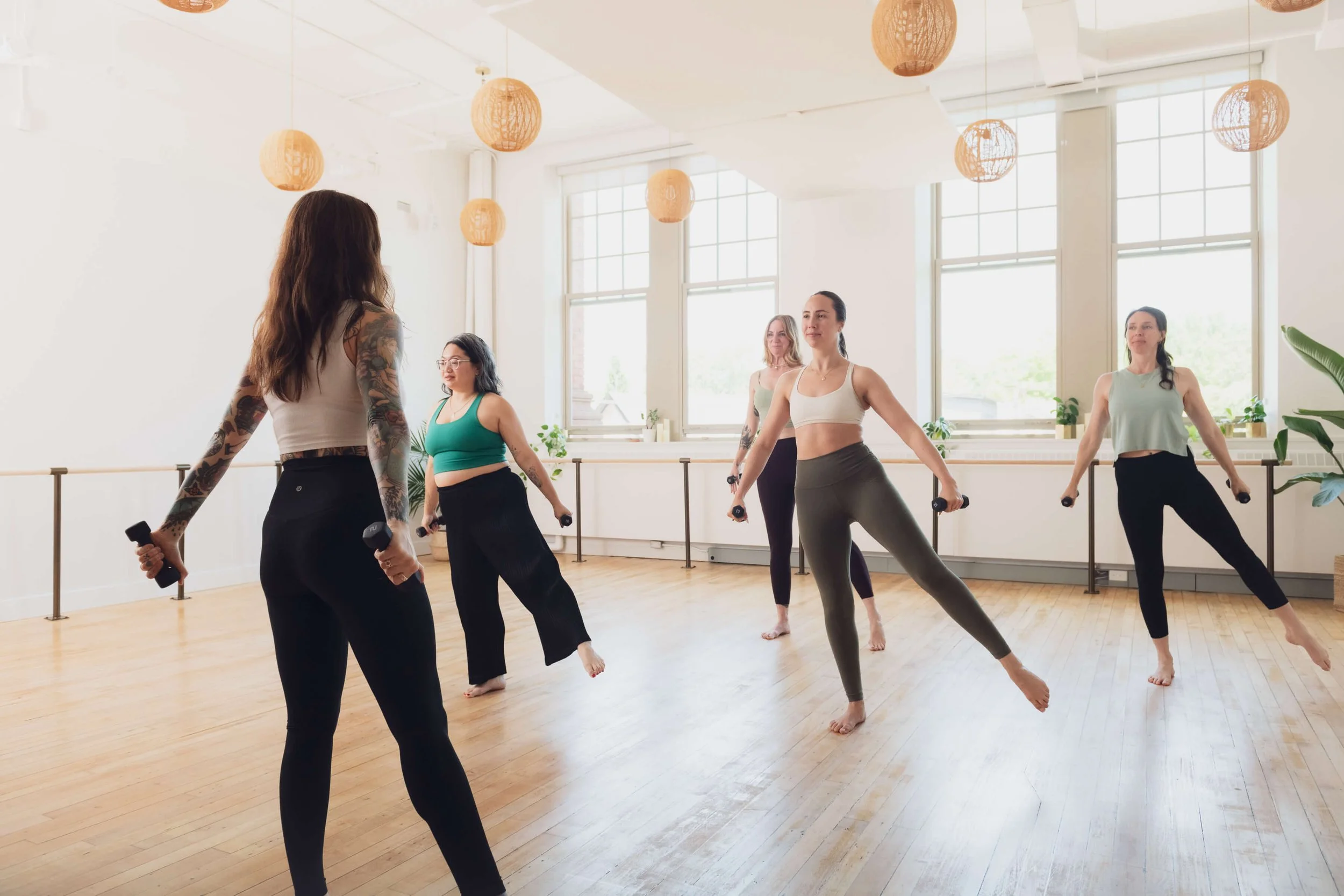 Women participating in a dance fitness class in a bright, spacious studio with large windows and wooden floors.