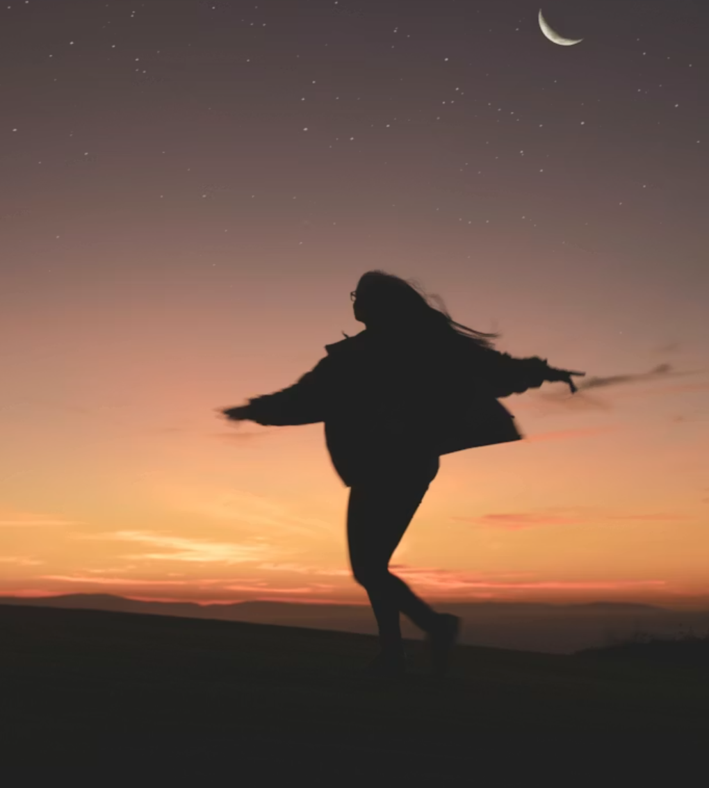 Silhouette of a woman dancing outdoors at sunset with a starry sky and crescent moon in the background.