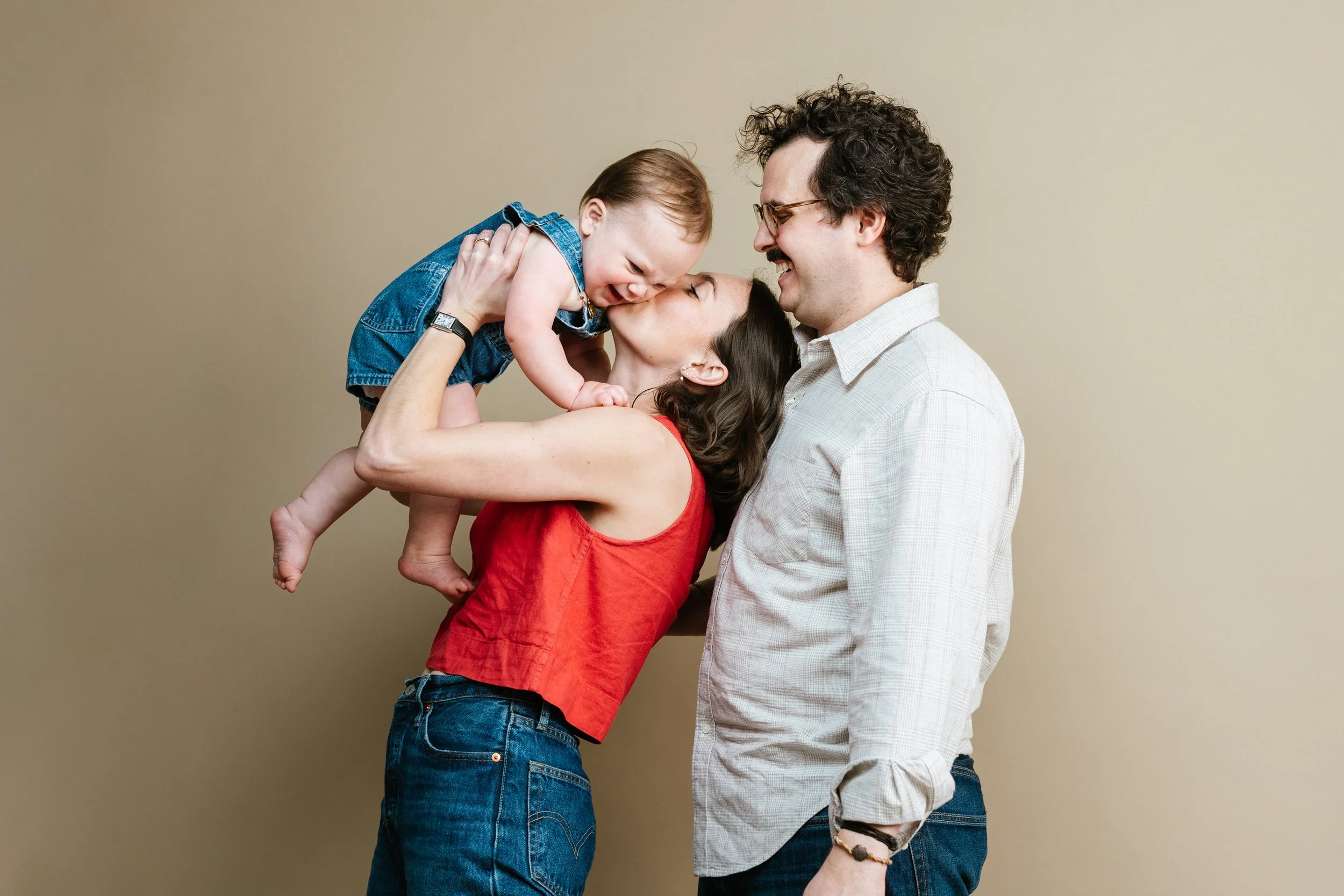 A family with a mother, father, and young daughter sharing a joyful moment together against a plain background.