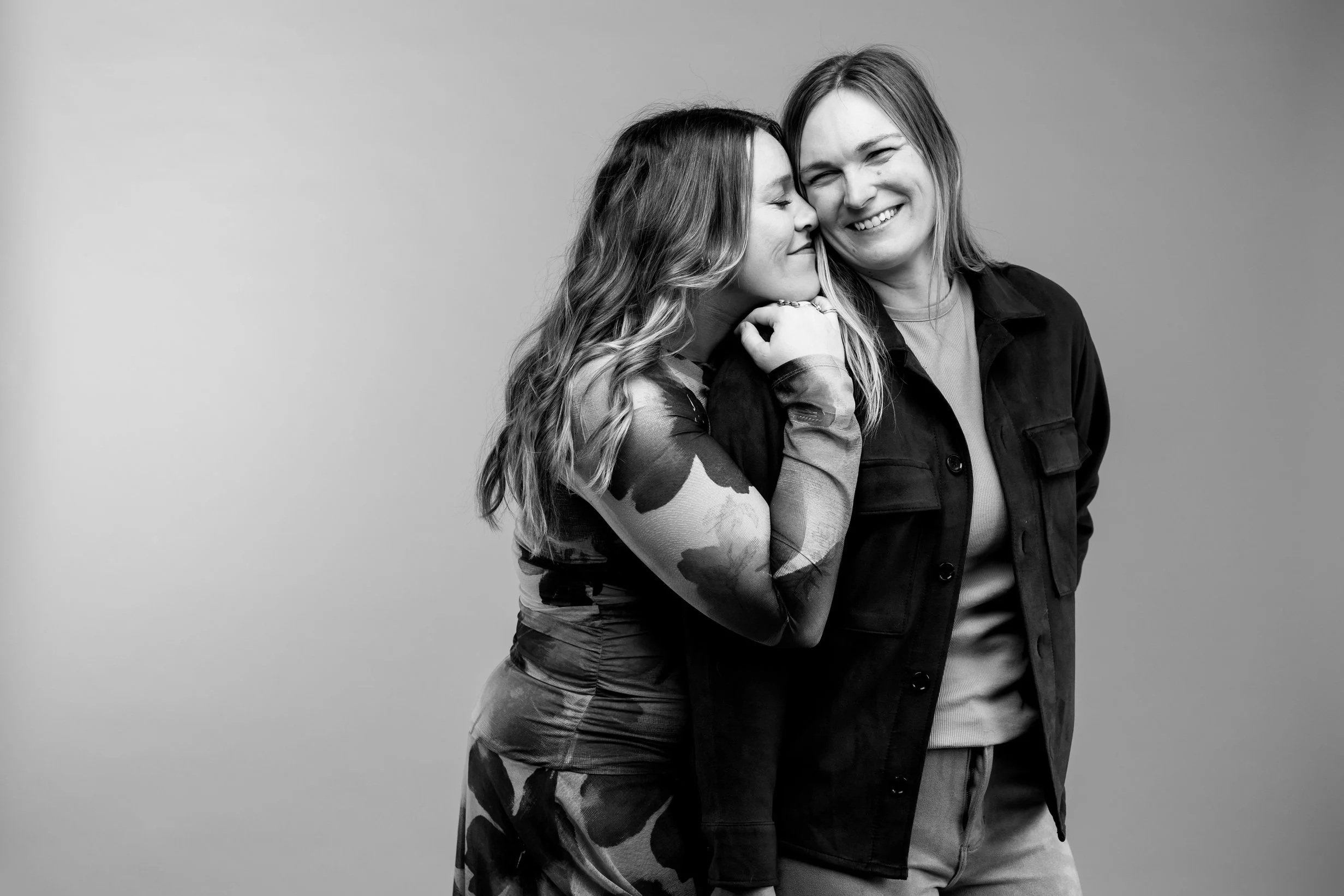 Two women hugging and smiling in a black-and-white photo against a plain background.