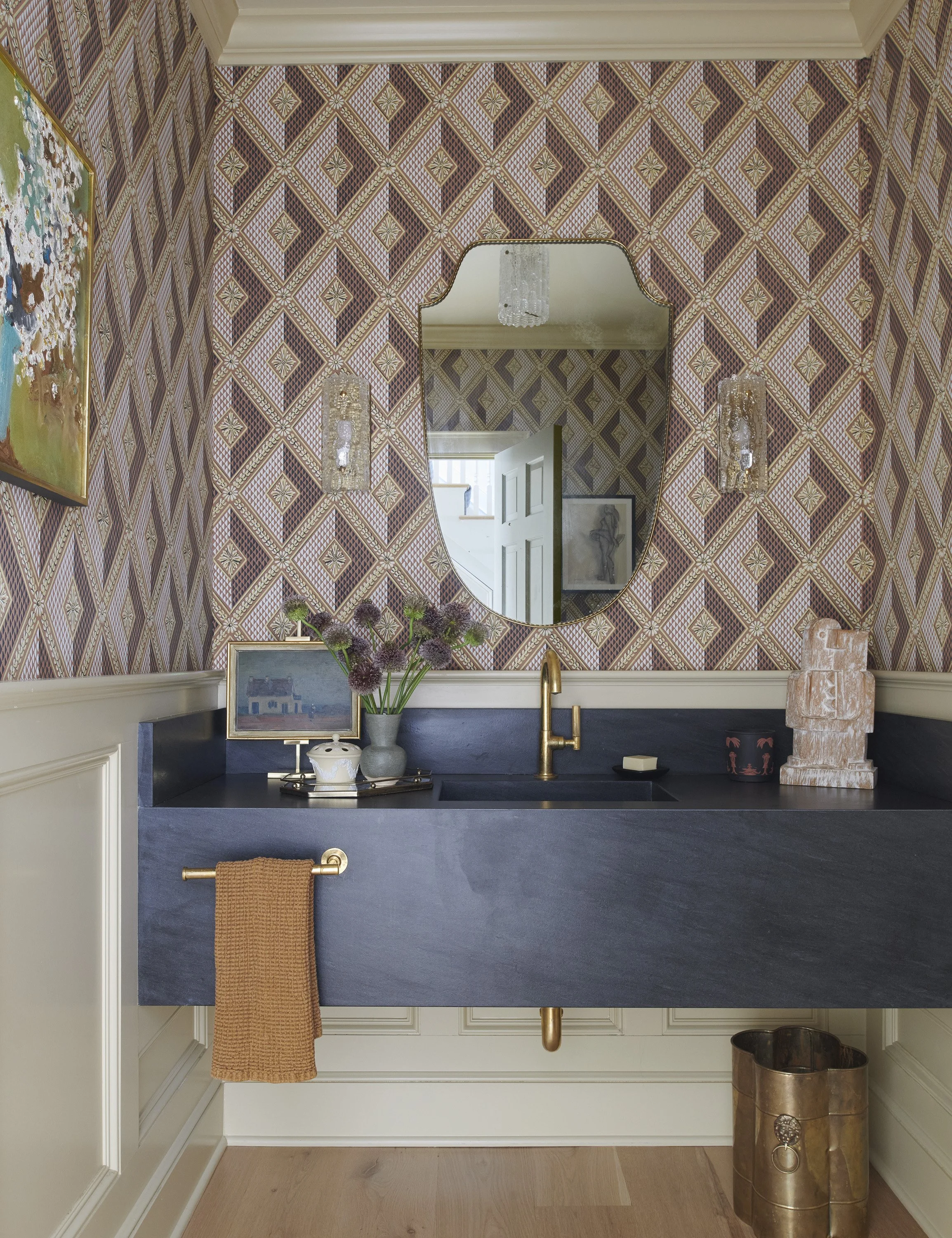 Stylish powder room with geometric wallpaper, dark floating vanity, brass fixtures, and decorative mirror.