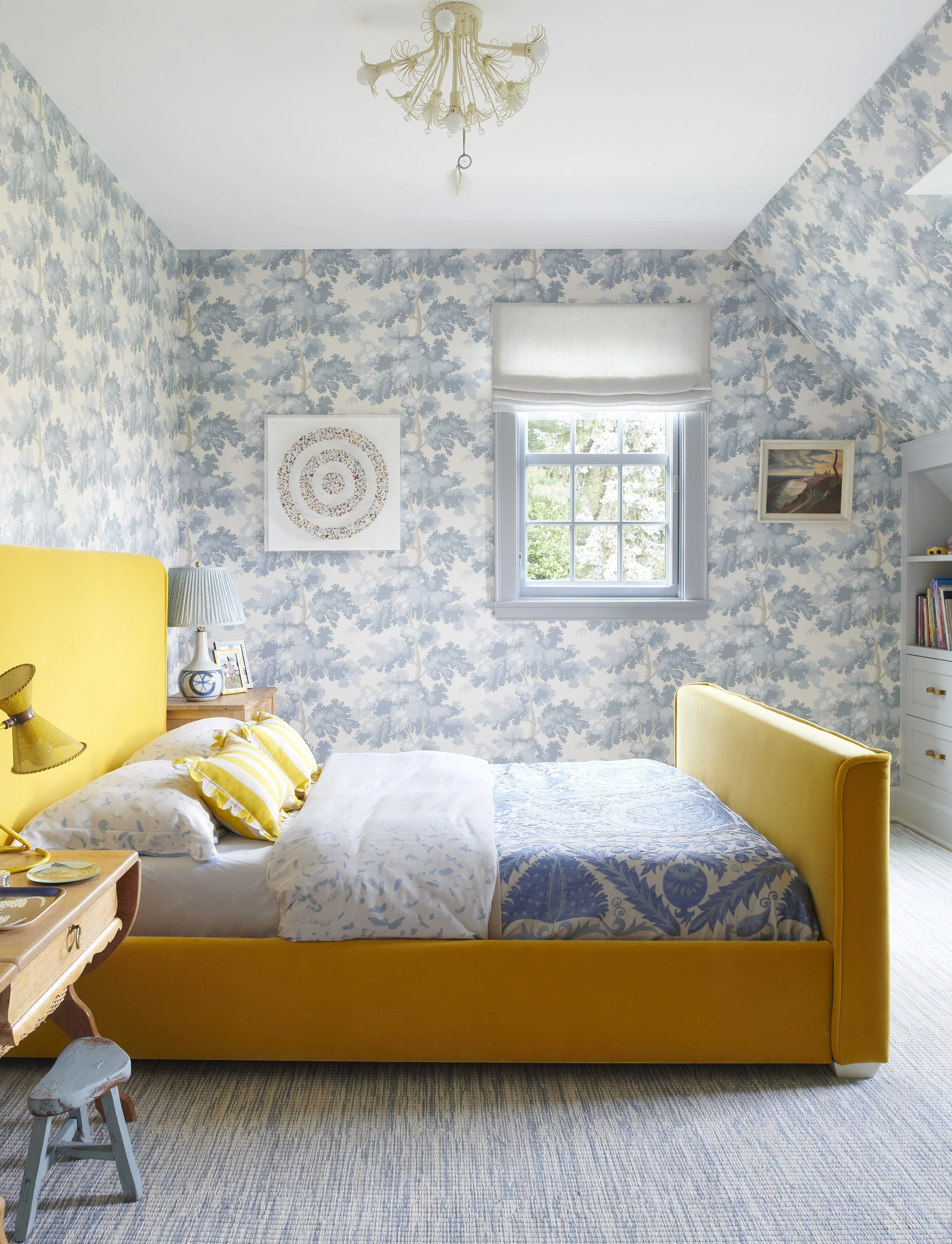 Bright bedroom with yellow upholstered bed, blue patterned wallpaper, and soft natural light.
