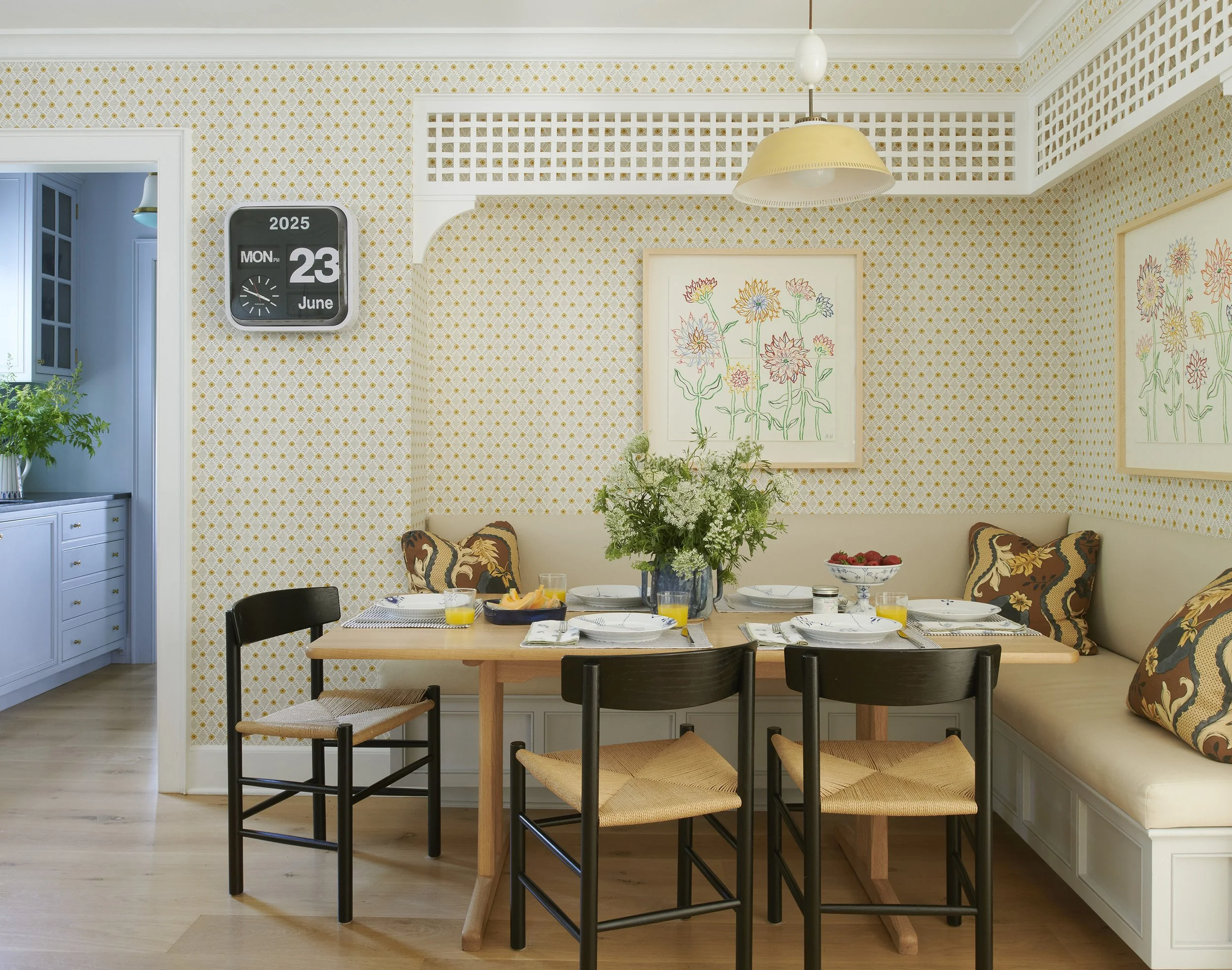 Elegant dining nook with built-in banquette, light wood table, black chairs, patterned wallpaper, and pendant lighting.
