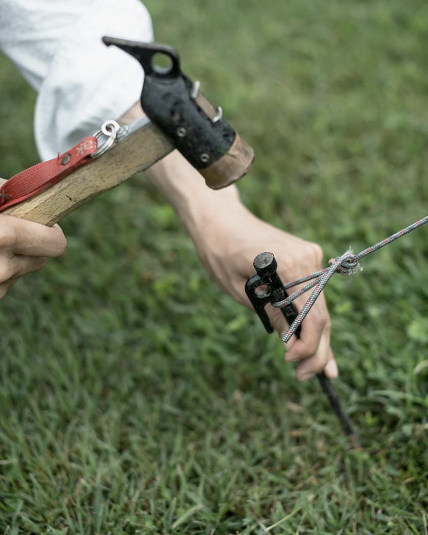 Close-up of a person hammering in a tent stake with the Snow Peak Copper Head Peg Hammer on grass.