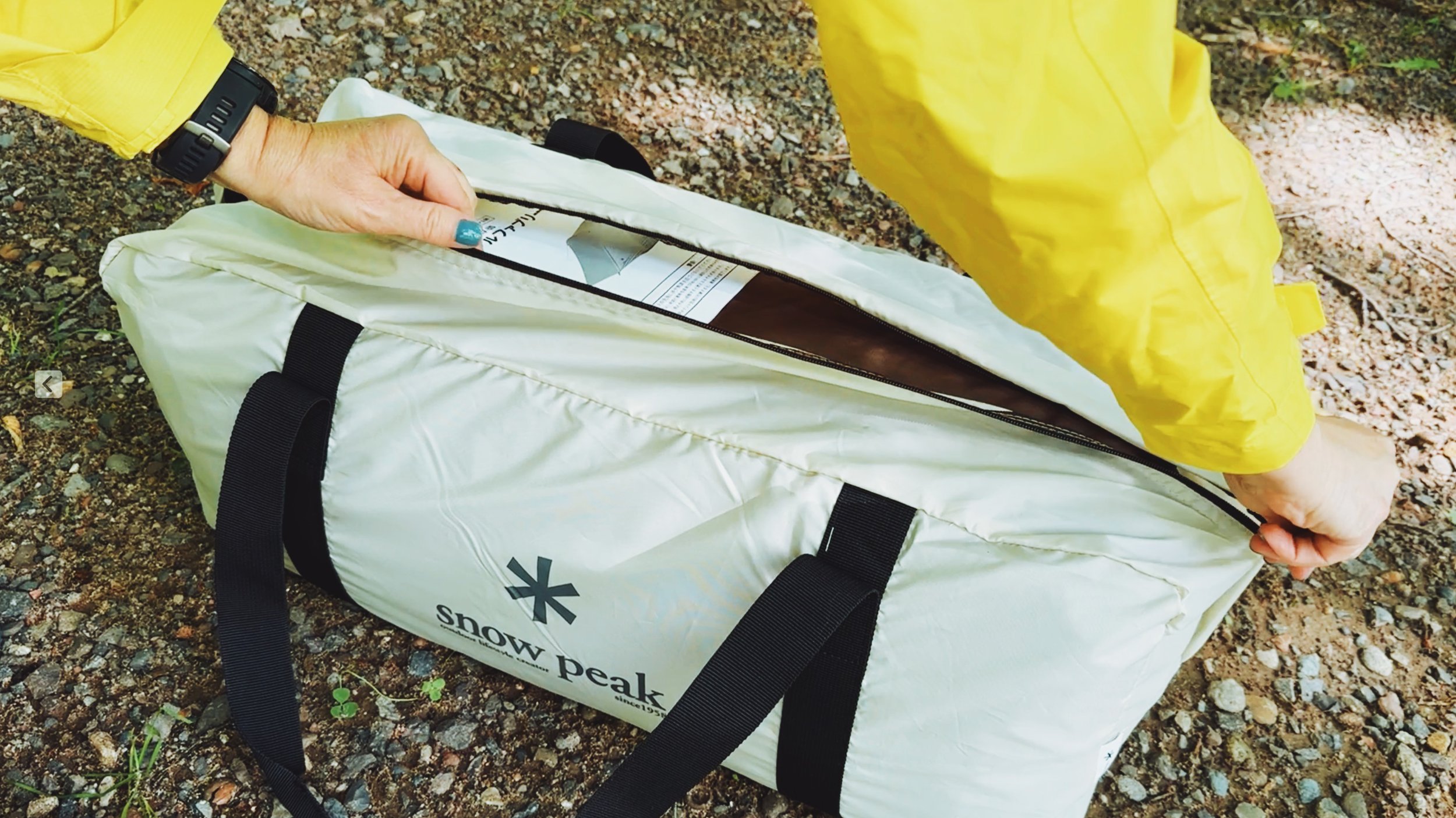 Close-up of a camper unzipping the Snow Peak Alpha Breeze Tent bag to reveal the tent and instruction sheet.