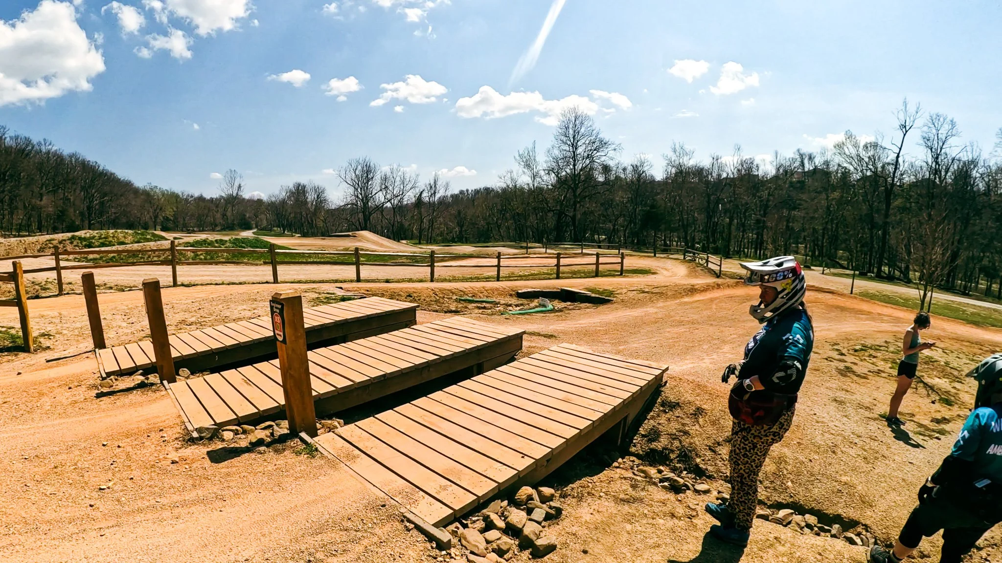 Mountain bikers standing near wooden skill progression features at the Slaughter Pen Skills Park in Bentonville, Arkansas.