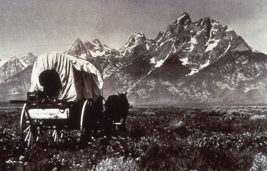 Early settlers in a covered wagon with the Tetons in the background.