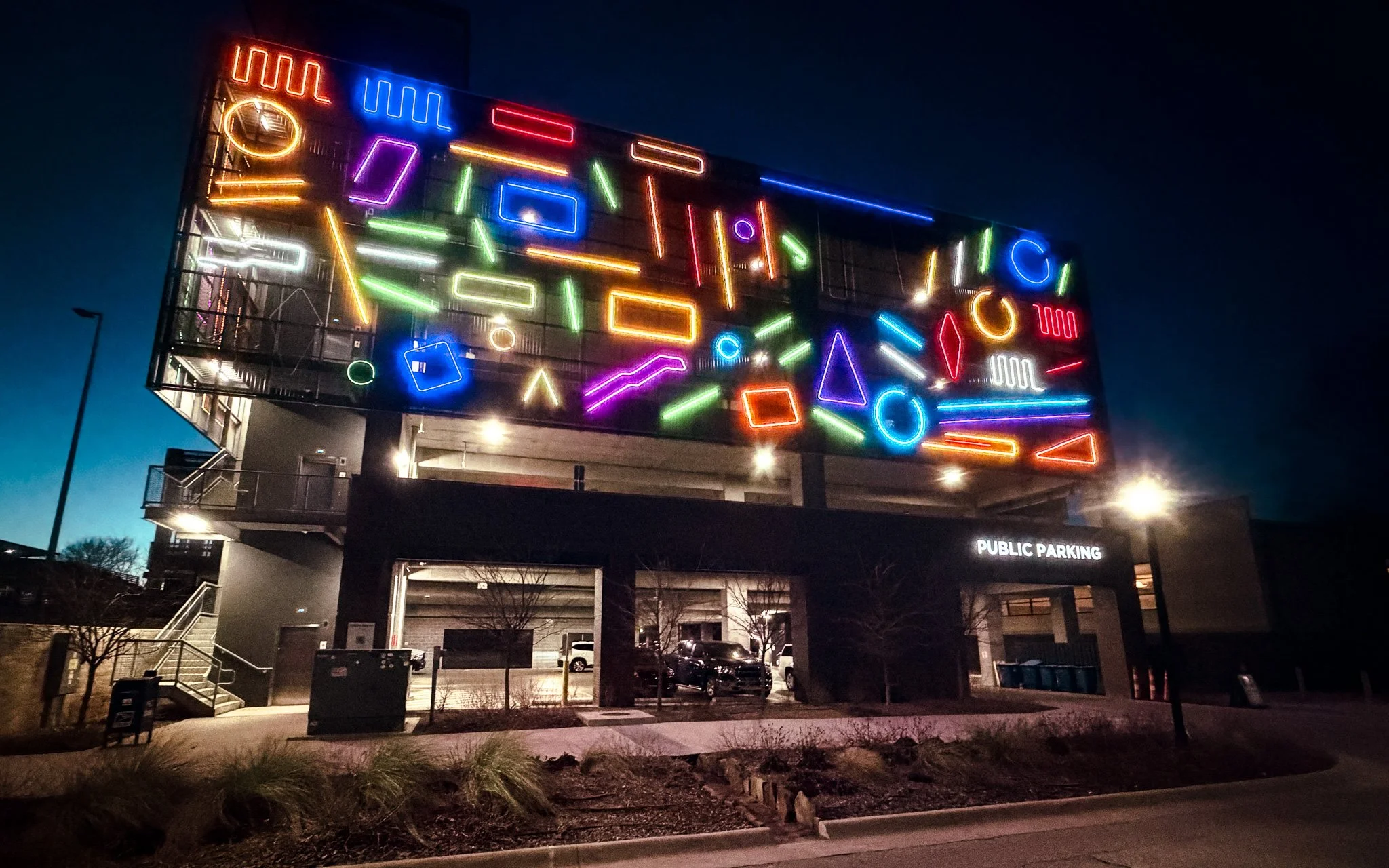 Colorful neon geometric shapes lighting up the exterior of the Walmart parking garage in downtown Bentonville at night.