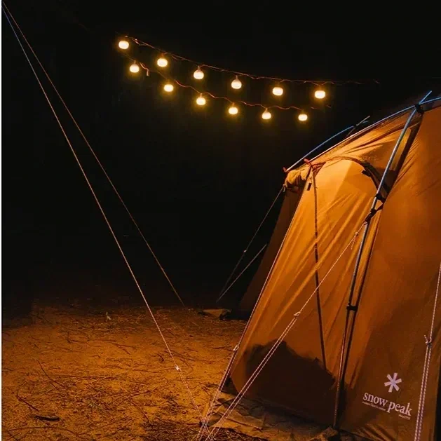 Snow Peak tent at night illuminated by warm Mini Hozuki string lights at a campsite
