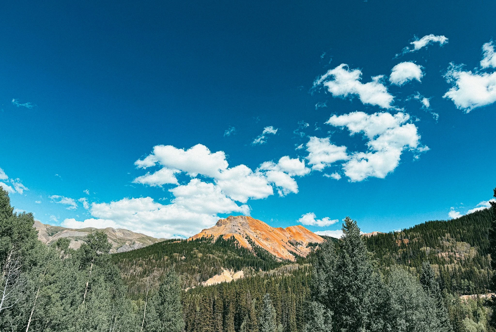 Red and orange mineral-stained Red Mountain rising above the forest near Red Mountain Pass in Colorado.