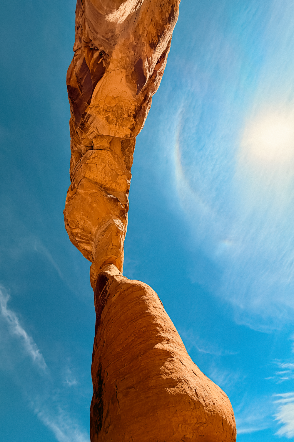 View looking upward beneath Delicate Arch showing sandstone structure and blue sky