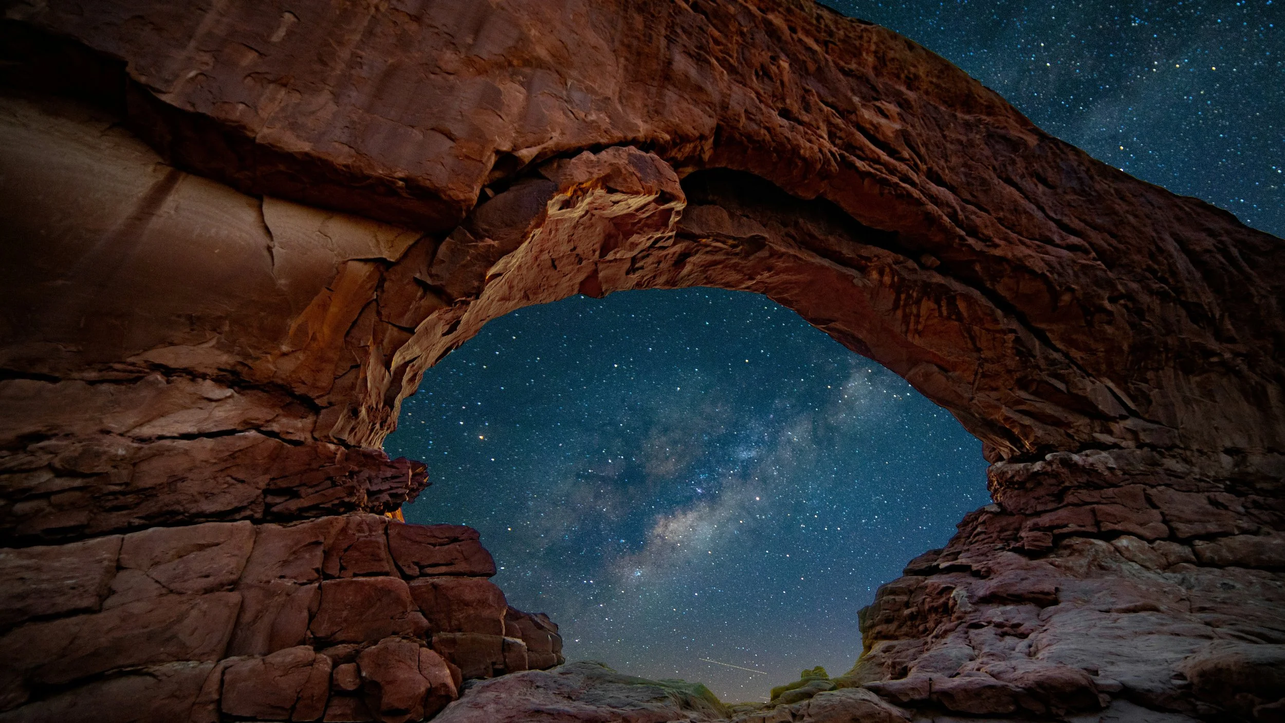 Milky Way visible through sandstone arch in the Windows section of Arches National Park Utah night sky