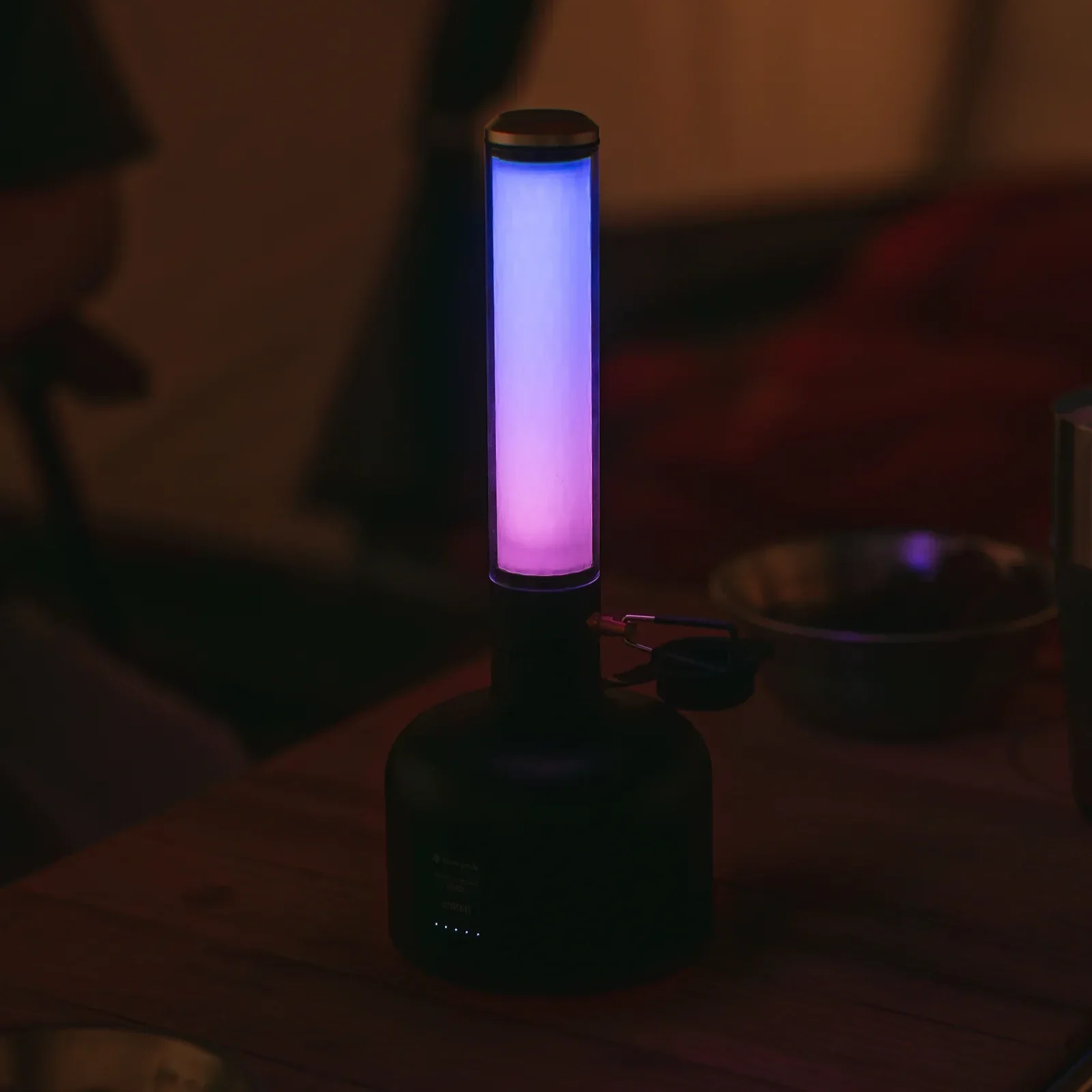 Snow Peak GigaPower Tabletop Lantern glowing with a blue and purple ambient light setting on a campsite table.