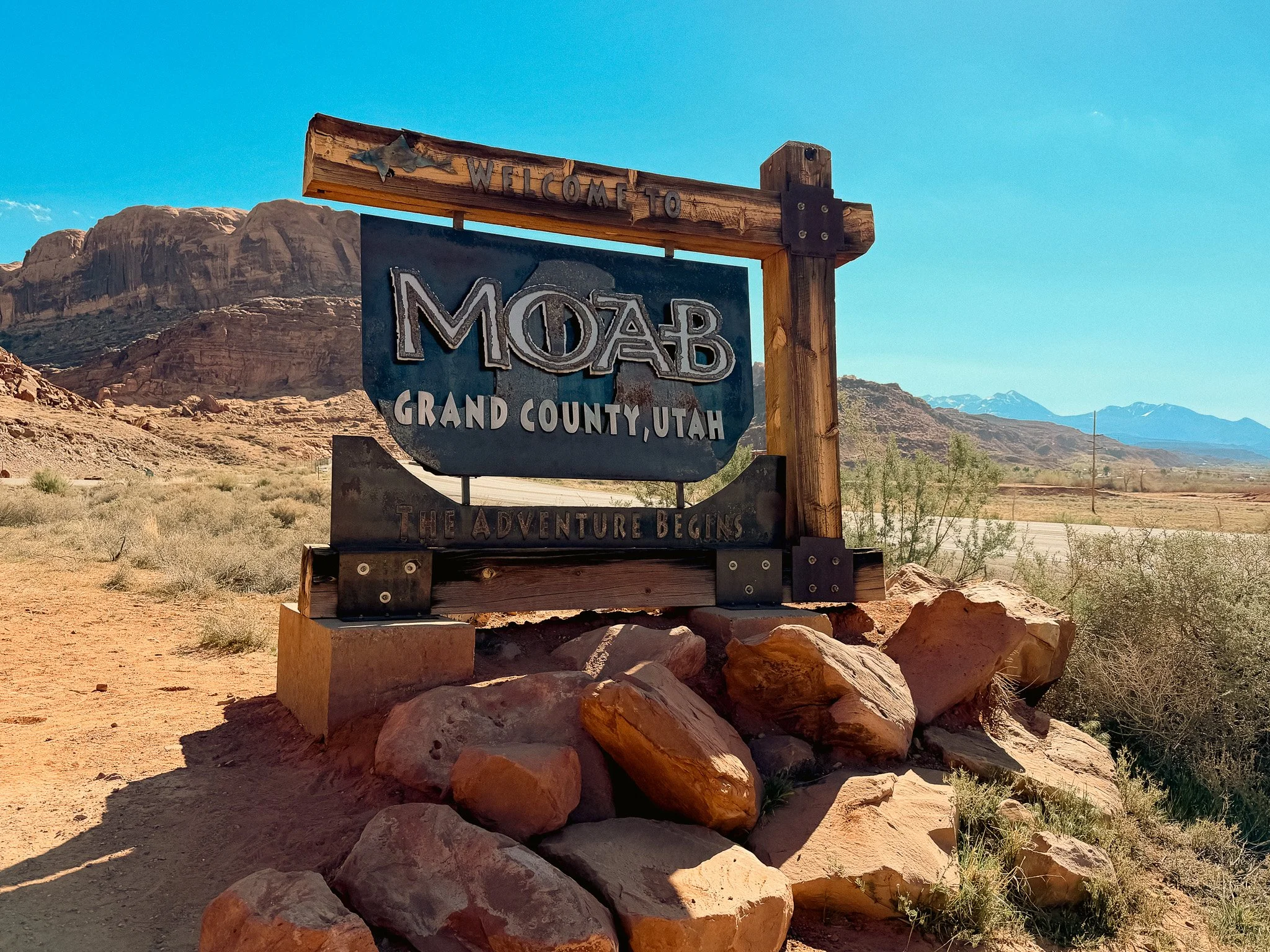 Welcome to Moab, Grand County, Utah sign surrounded by red sandstone formations and desert mountains.