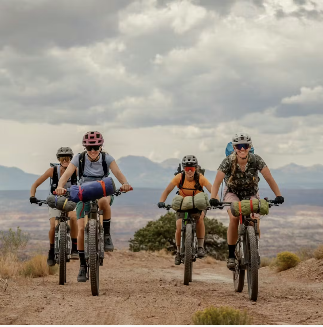 Group of women mountain biking on a dirt trail with gear packs and helmets