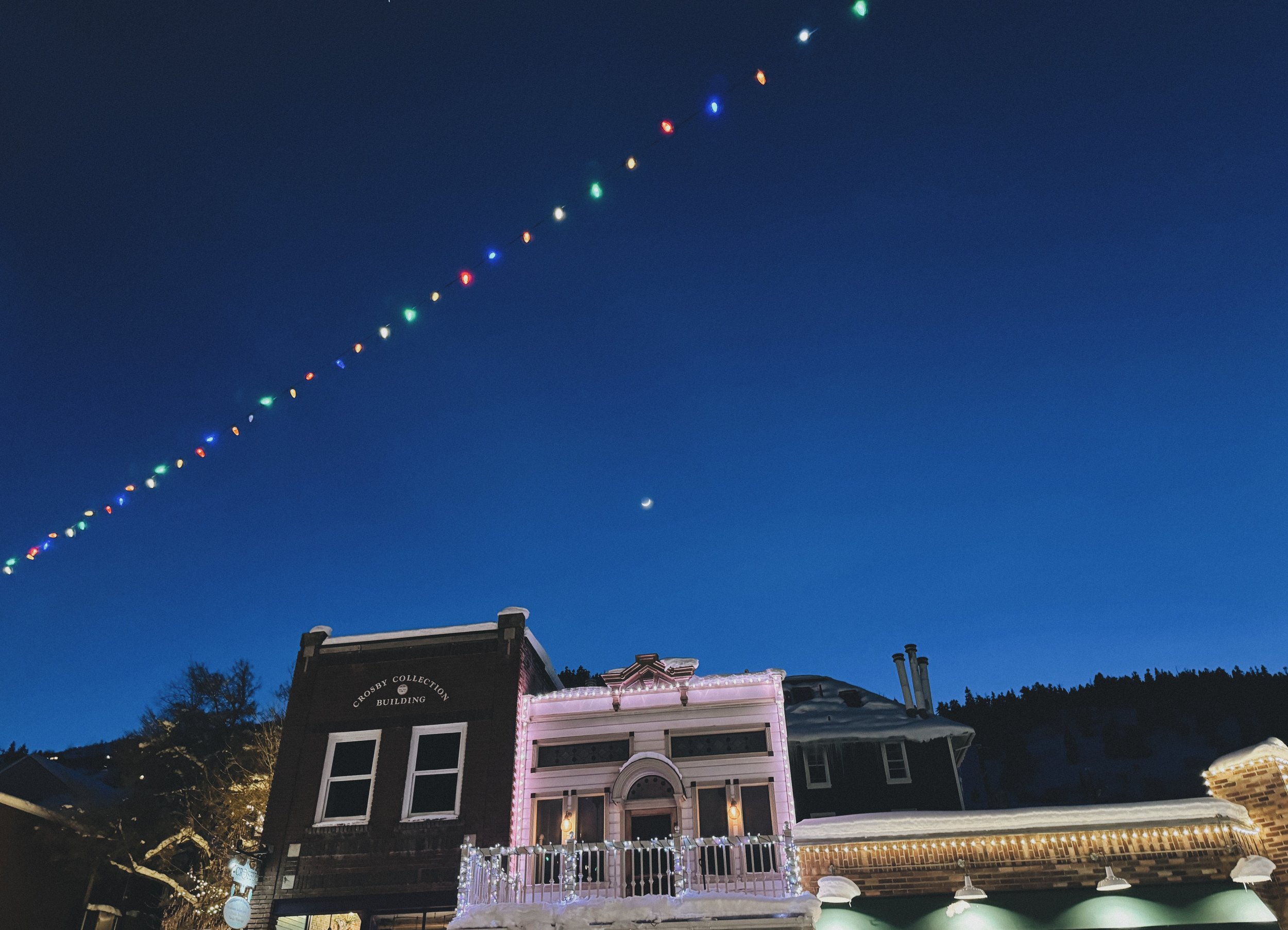 View of two building tops on Main Street at night with a string of colorful lights suspended high above, set against a clear night sky