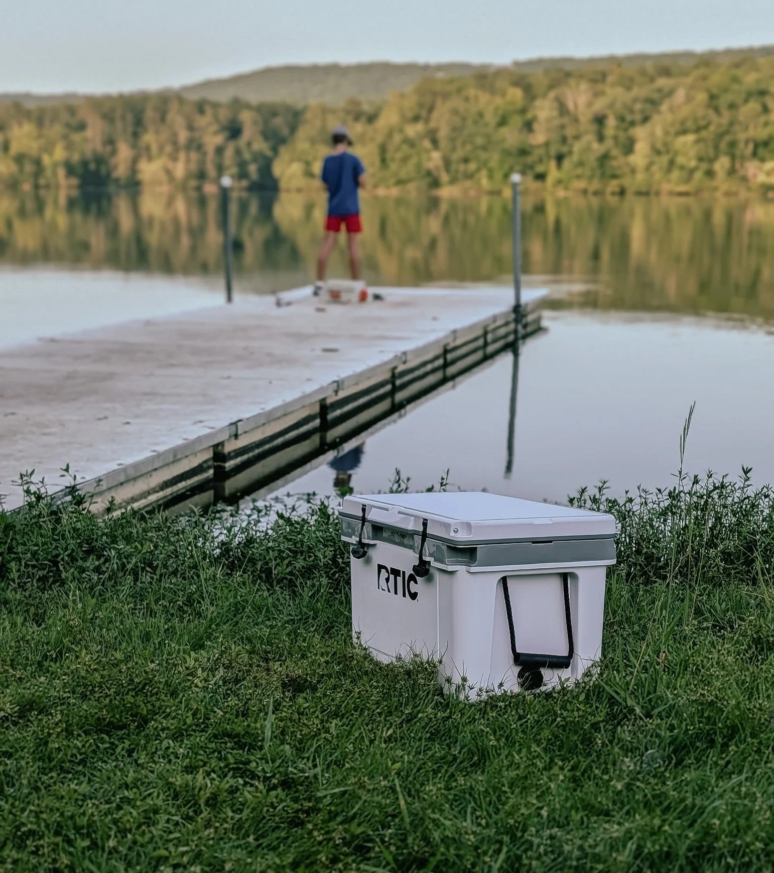RTIC 32 QT Ultra-Light Cooler sitting beside a lake with a dock in the background.