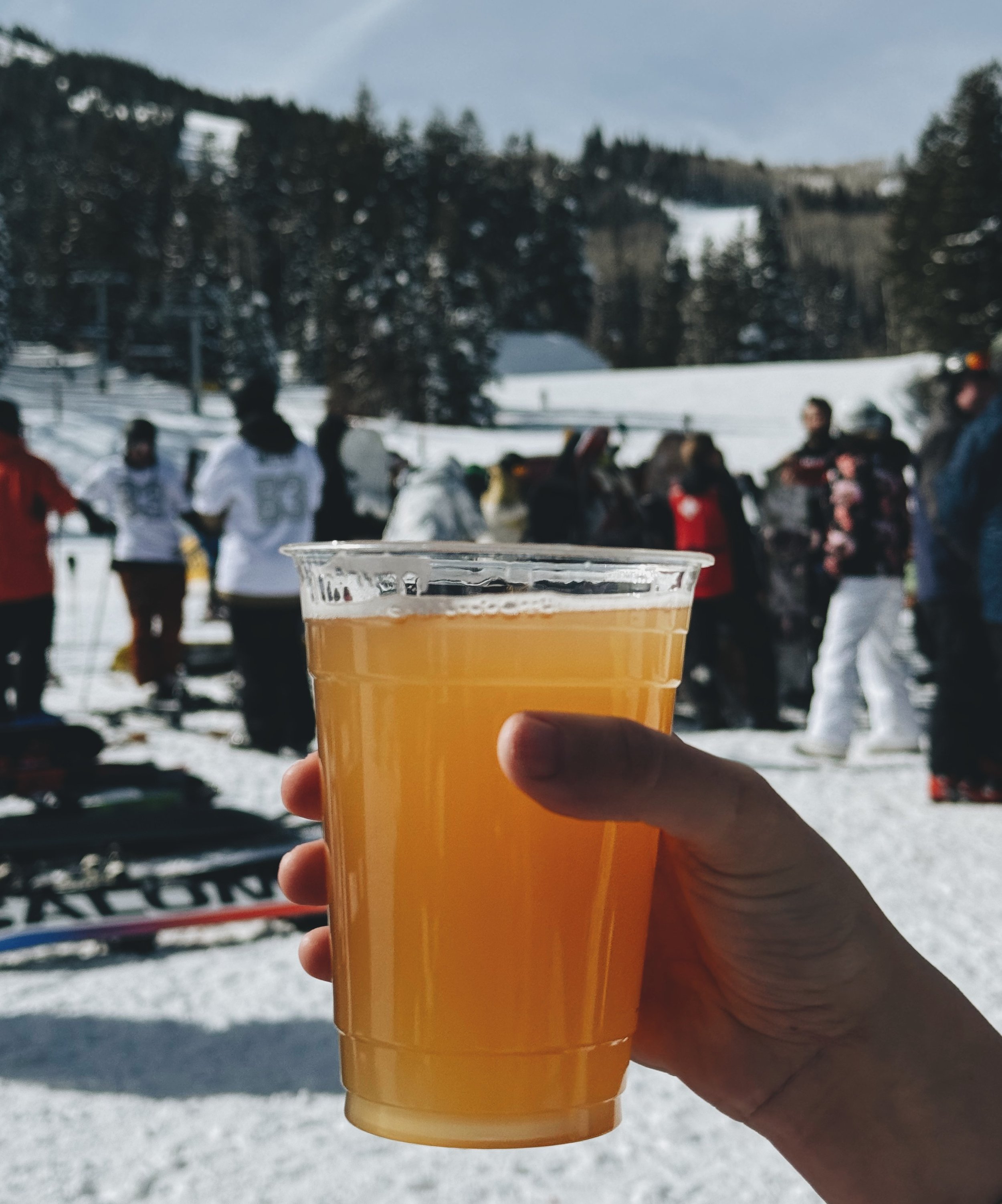 A refreshing beer at Tombstone BBQ, set against a backdrop of skiers relaxing in the snow on a sunny blue-sky day in Park City.
