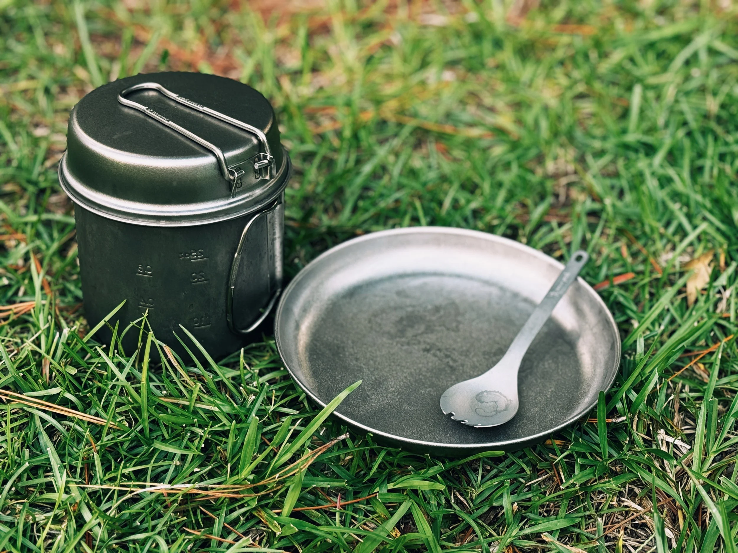 Snow Peak titanium plate, spork, and cook set resting on grass at a campsite
