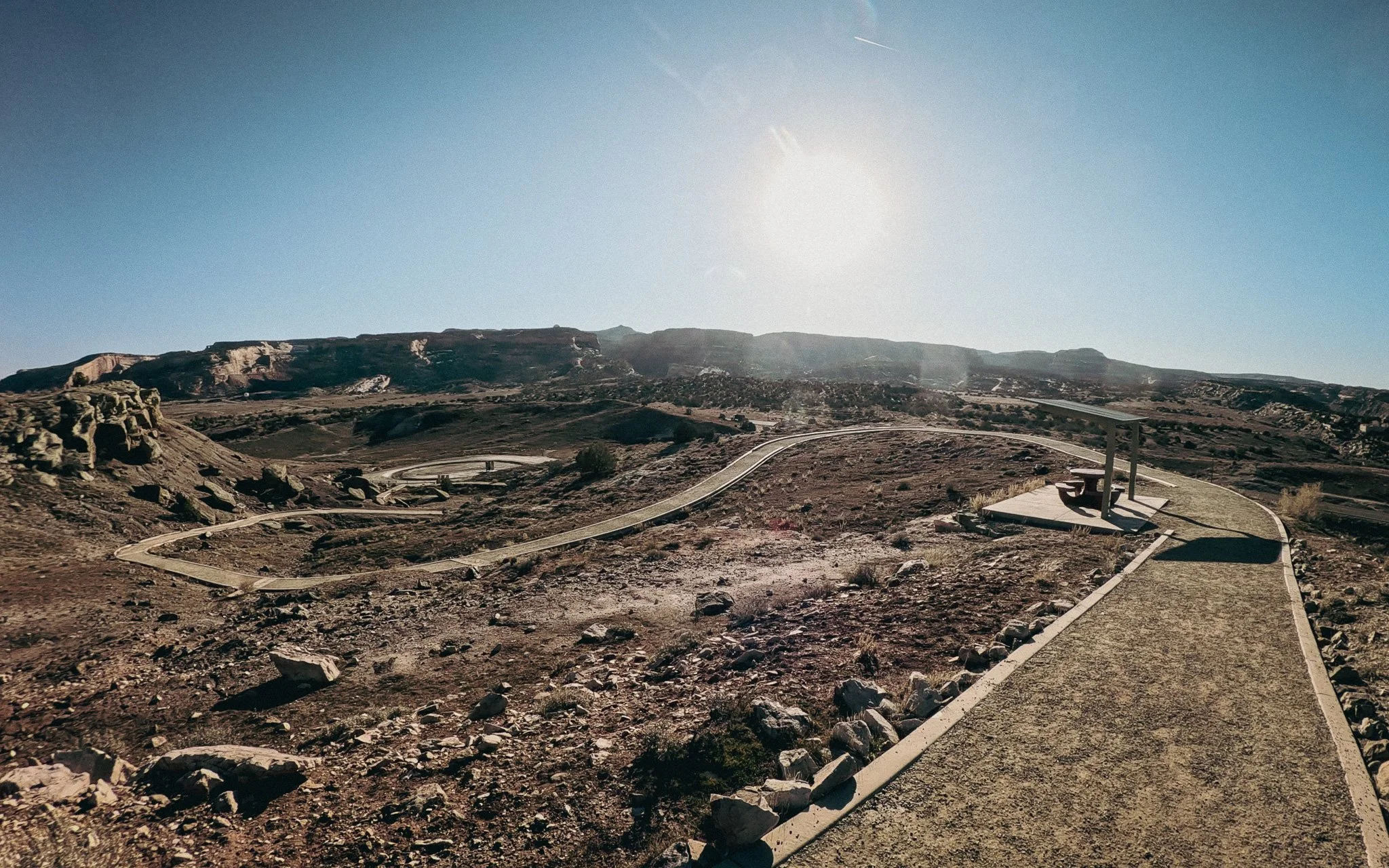 Paved walking path and overlook bench at Dinosaur Hill fossil site in Fruita, Colorado with desert mesas in the distance.