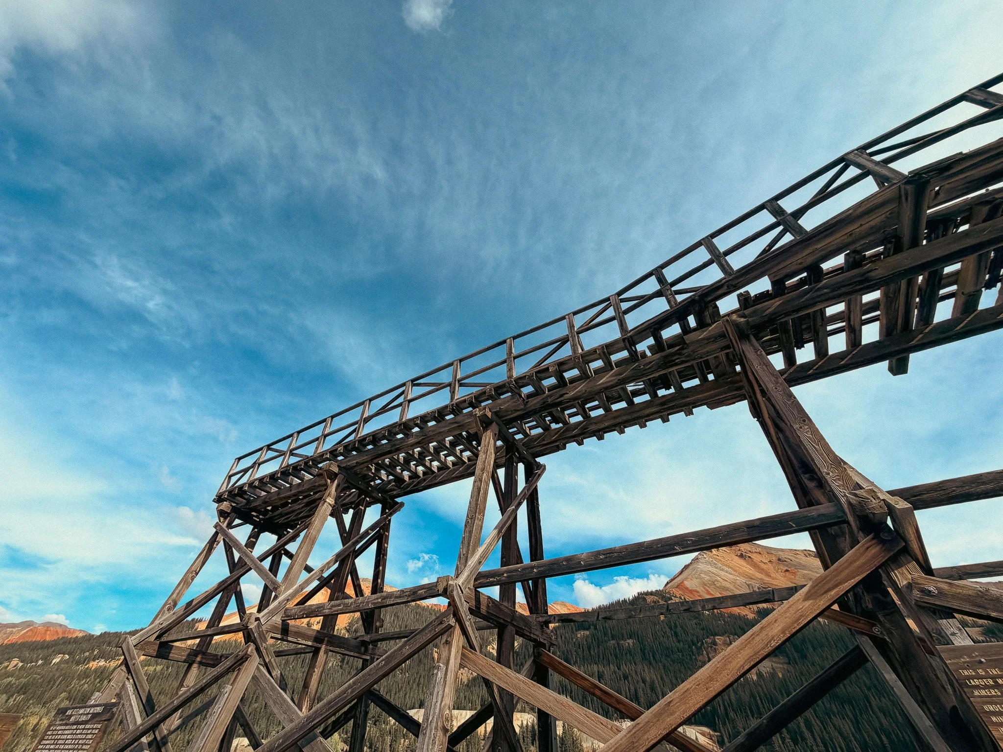 Looking up at the weathered wooden tram structure at the Yankee Girl Mine near Red Mountain Pass, with red-streaked mountains in the background.