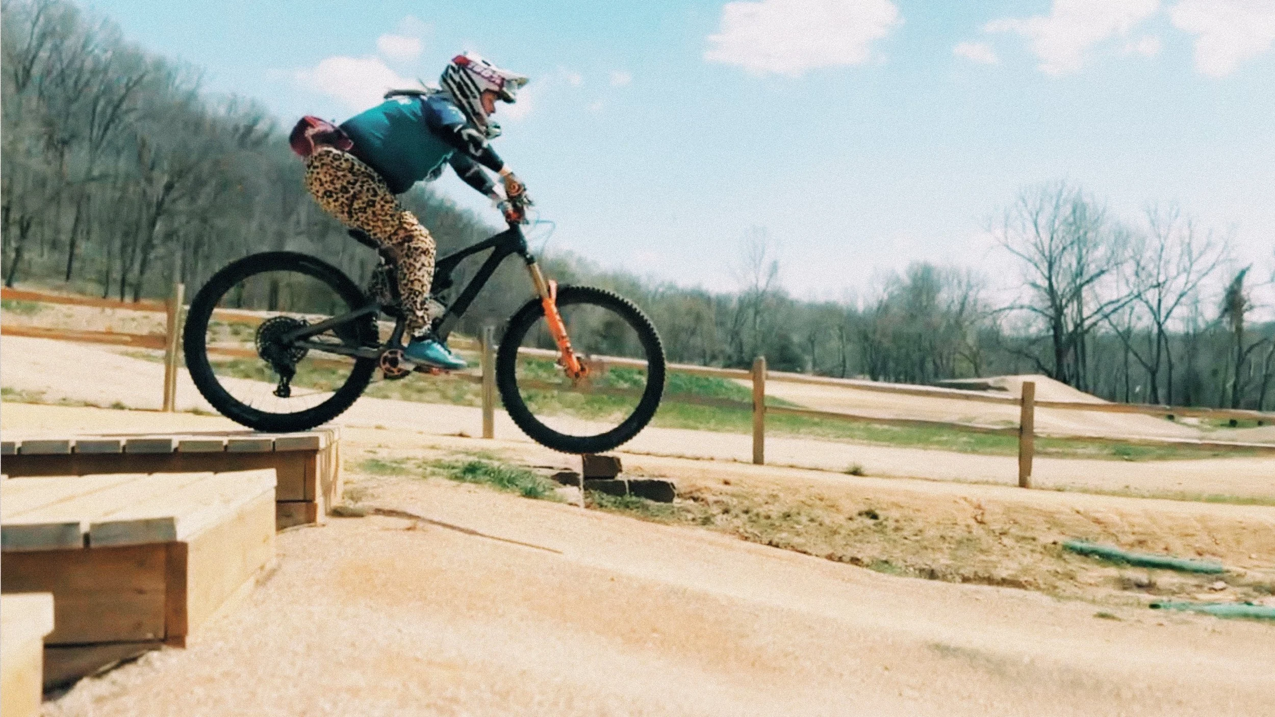 Mountain biker riding a wooden feature at the Slaughter Pen skills park in Bentonville on a clear day.
