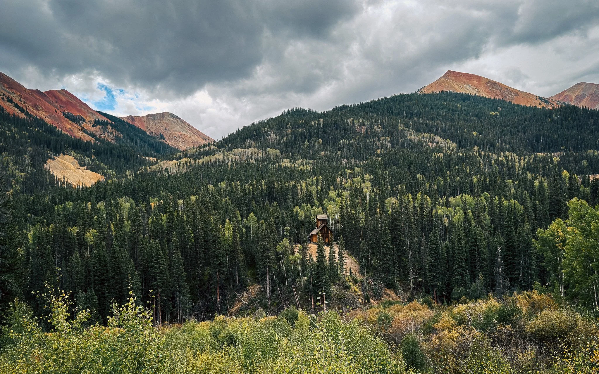 Historic Colorado Boy Mine surrounded by forest and red mountain peaks in the San Juan Mountains near Ouray, Colorado.