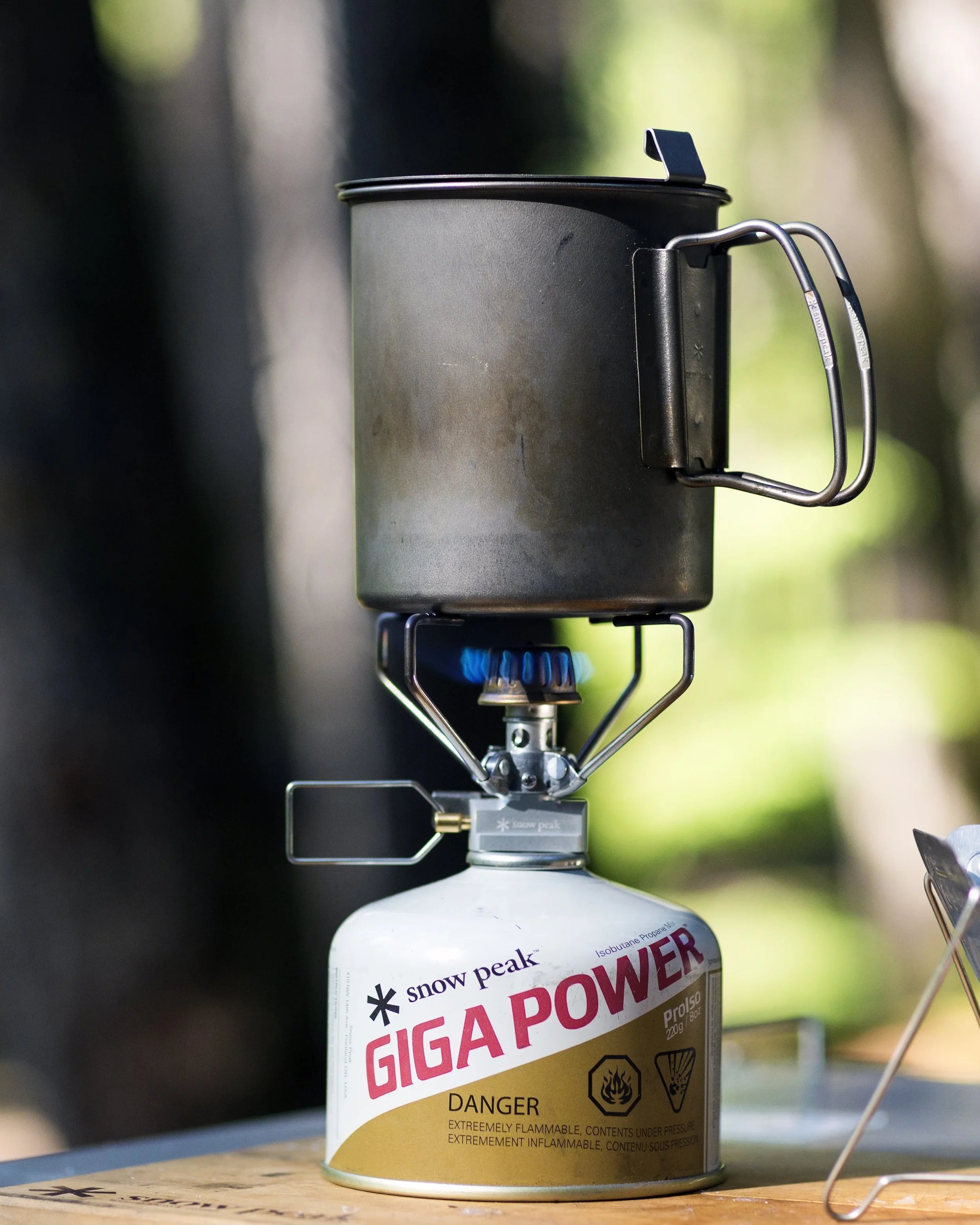 Snow Peak Trek 700 titanium cook pot heating on a GigaPower stove with blue flame at a campsite