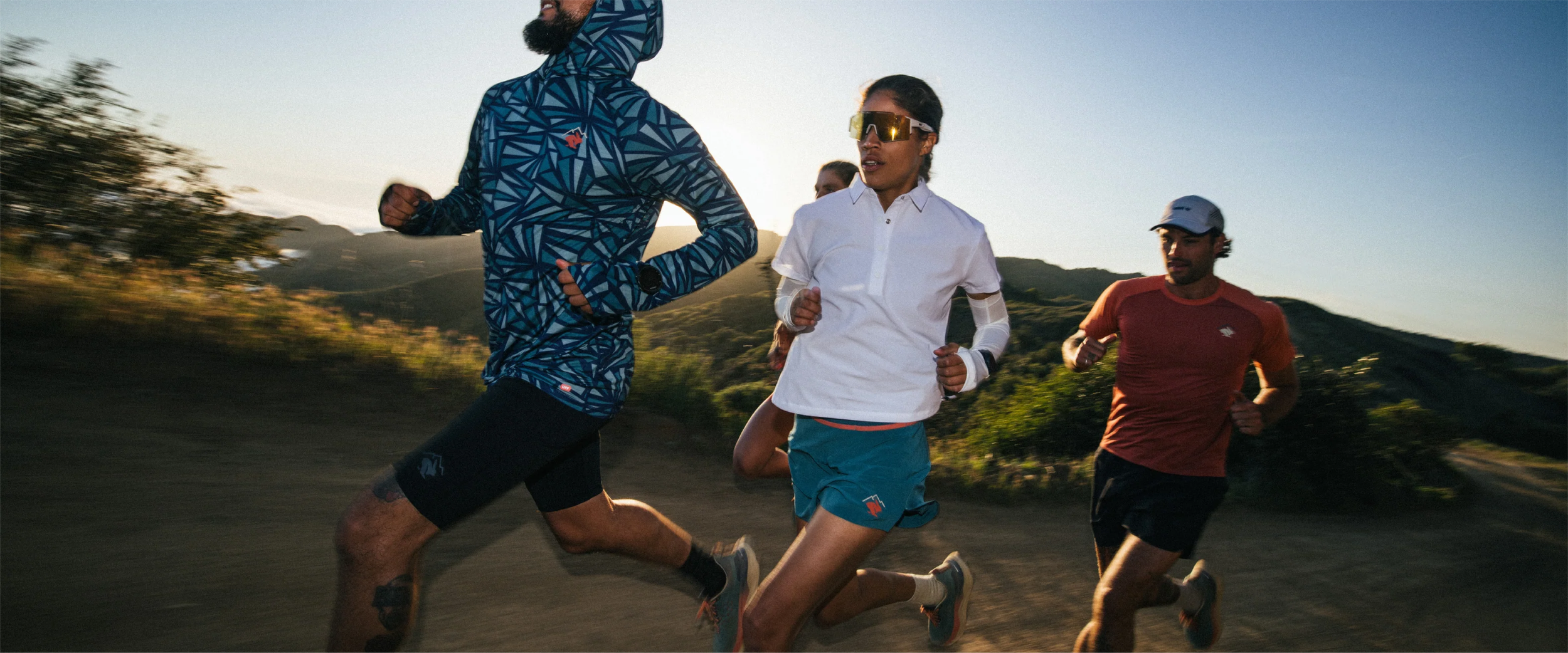 trail runners wearing rabbit running shorts, performance tees, and rabbit running shoes on mountain trail at sunset