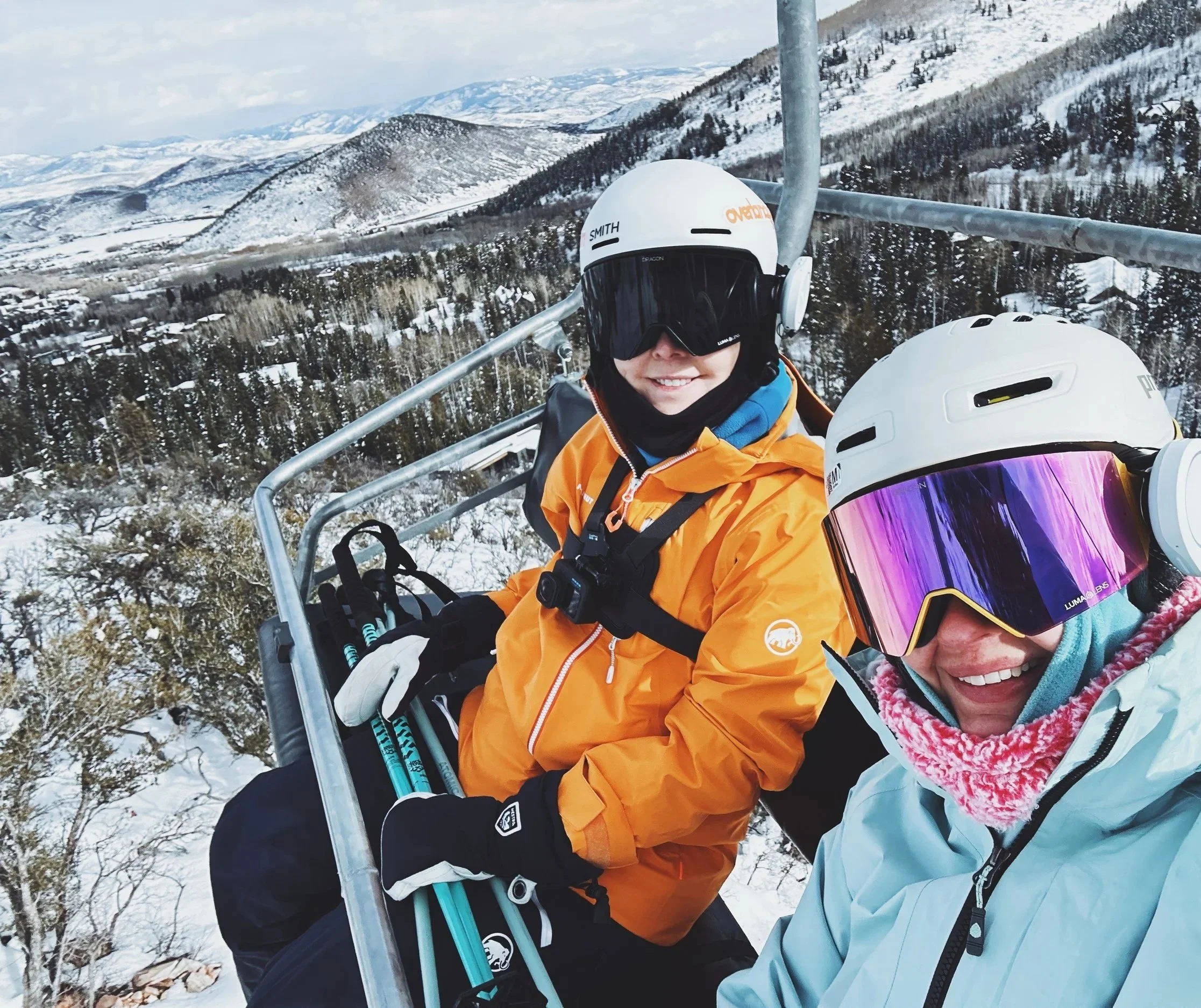 Wearing black and white Hestra Heli Ski Mittens while riding a chairlift with a friend in the snowy mountains.