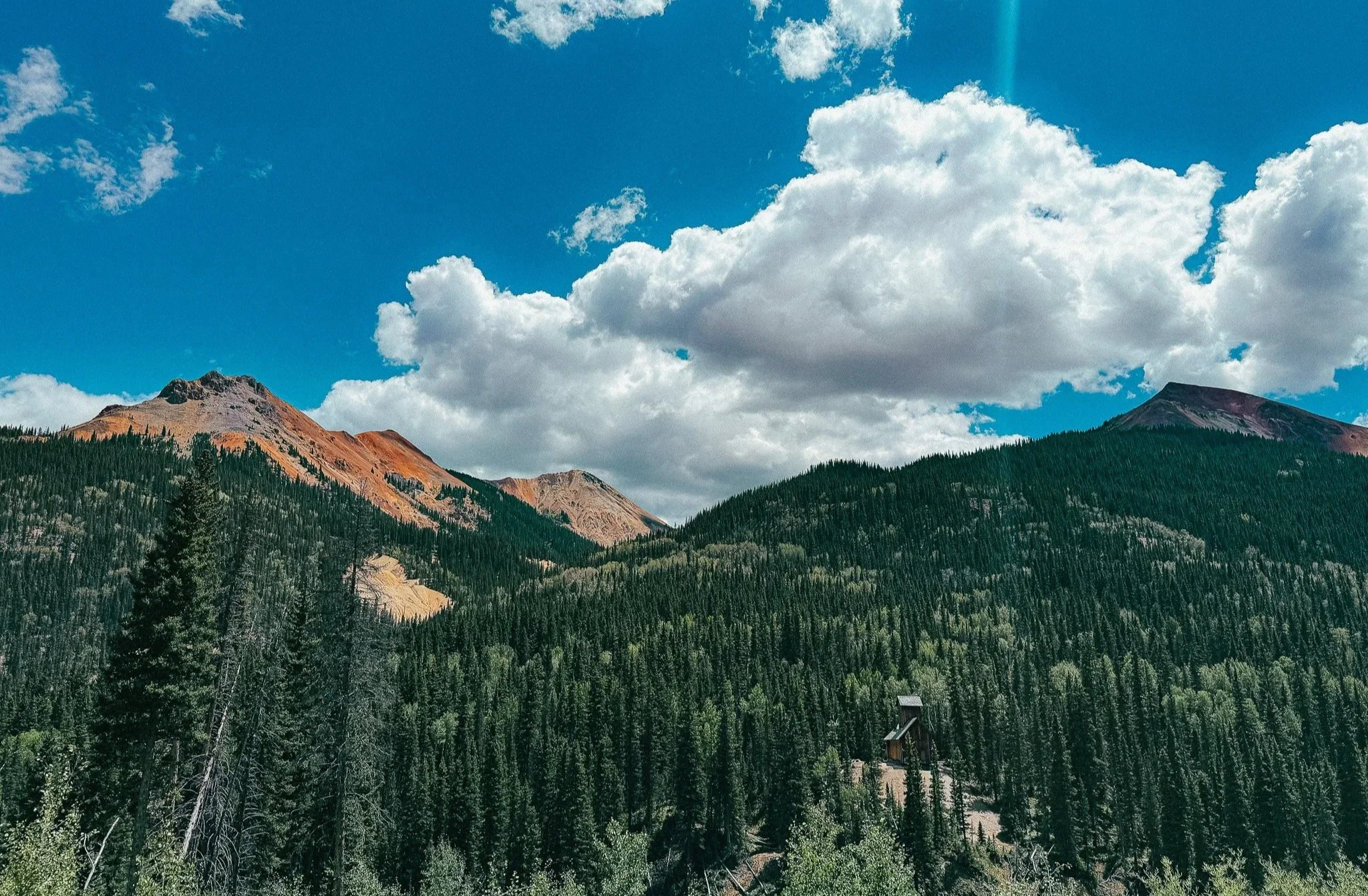 Historic mining structure below red and orange mountains along the Million Dollar Highway in Colorado.