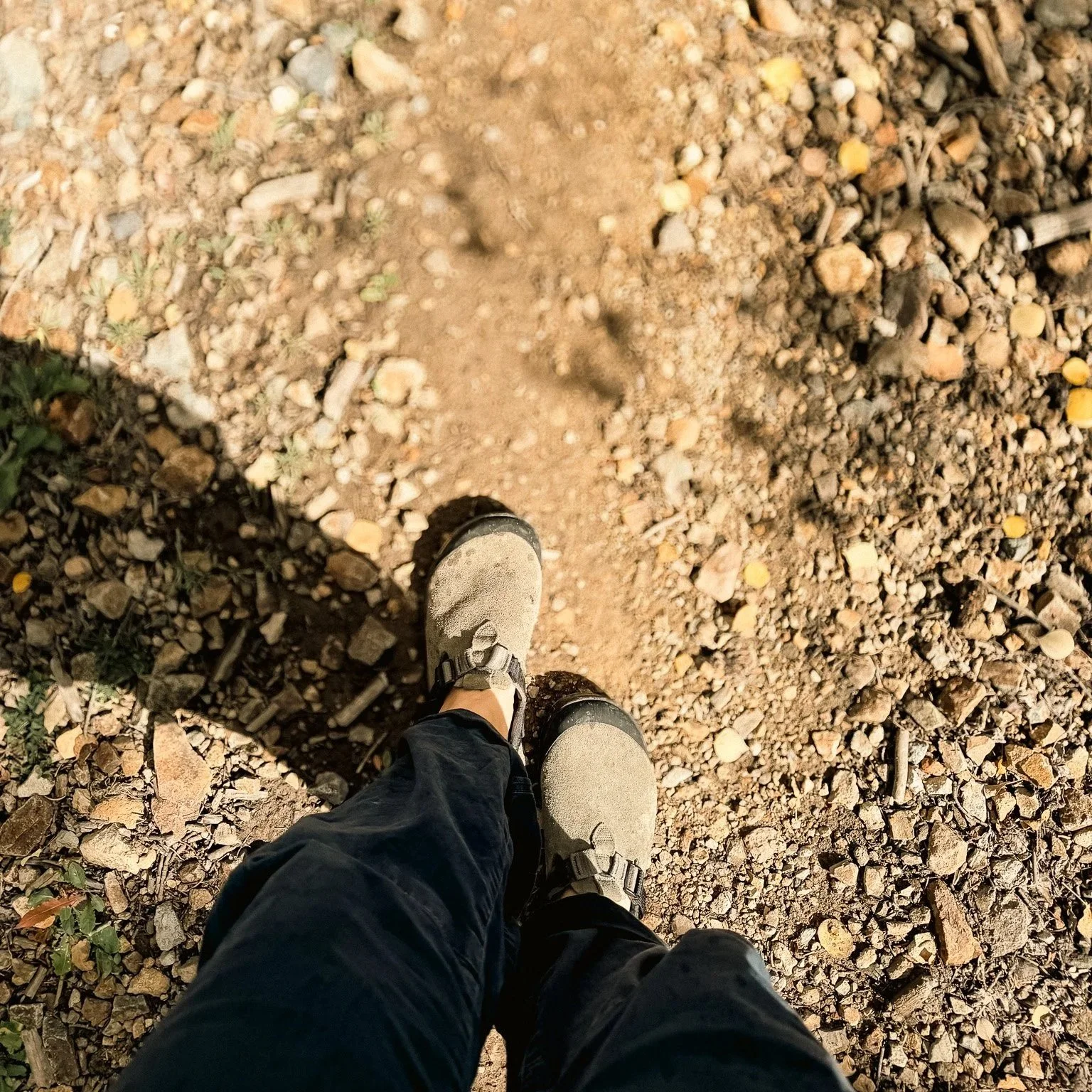 Walking along a rocky dirt trail wearing Sagebrush Bedrock Mountain Clogs with black hiking pants.