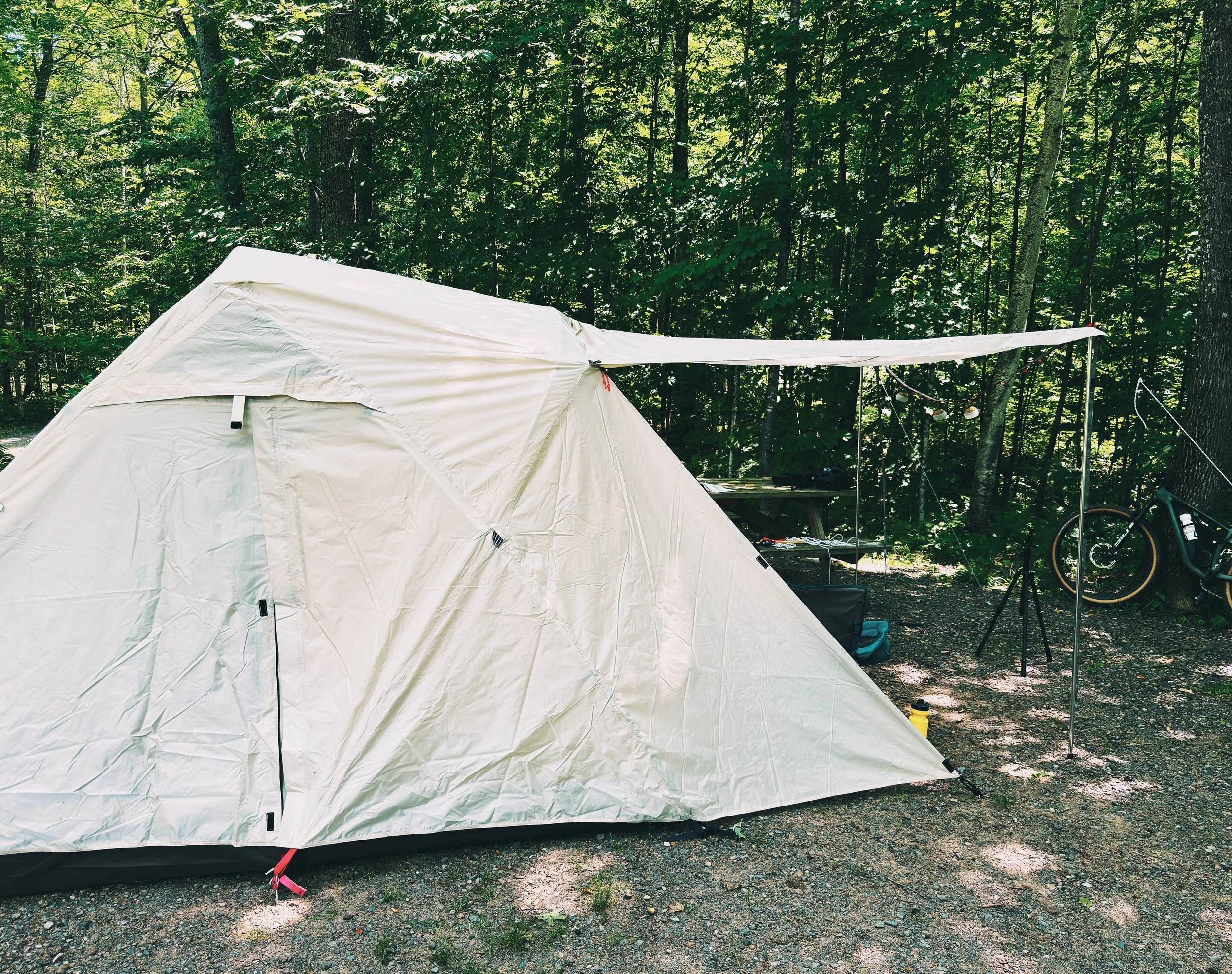 Snow Peak Alpha Breeze tent pitched at a wooded campsite with extended vestibule and gear setup nearby