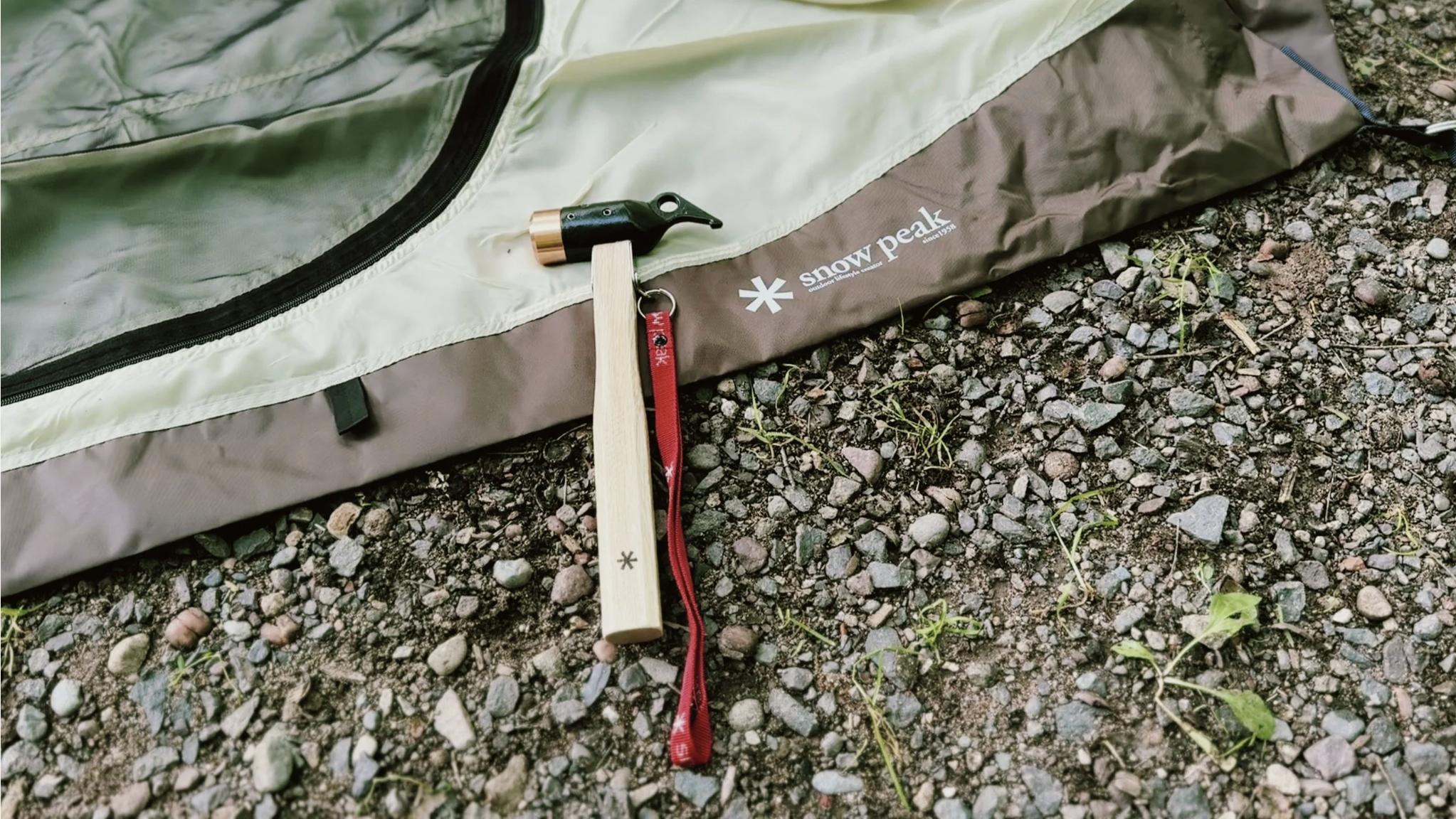 Snow Peak Copper Head Peg Hammer resting beside a tent on a campsite.