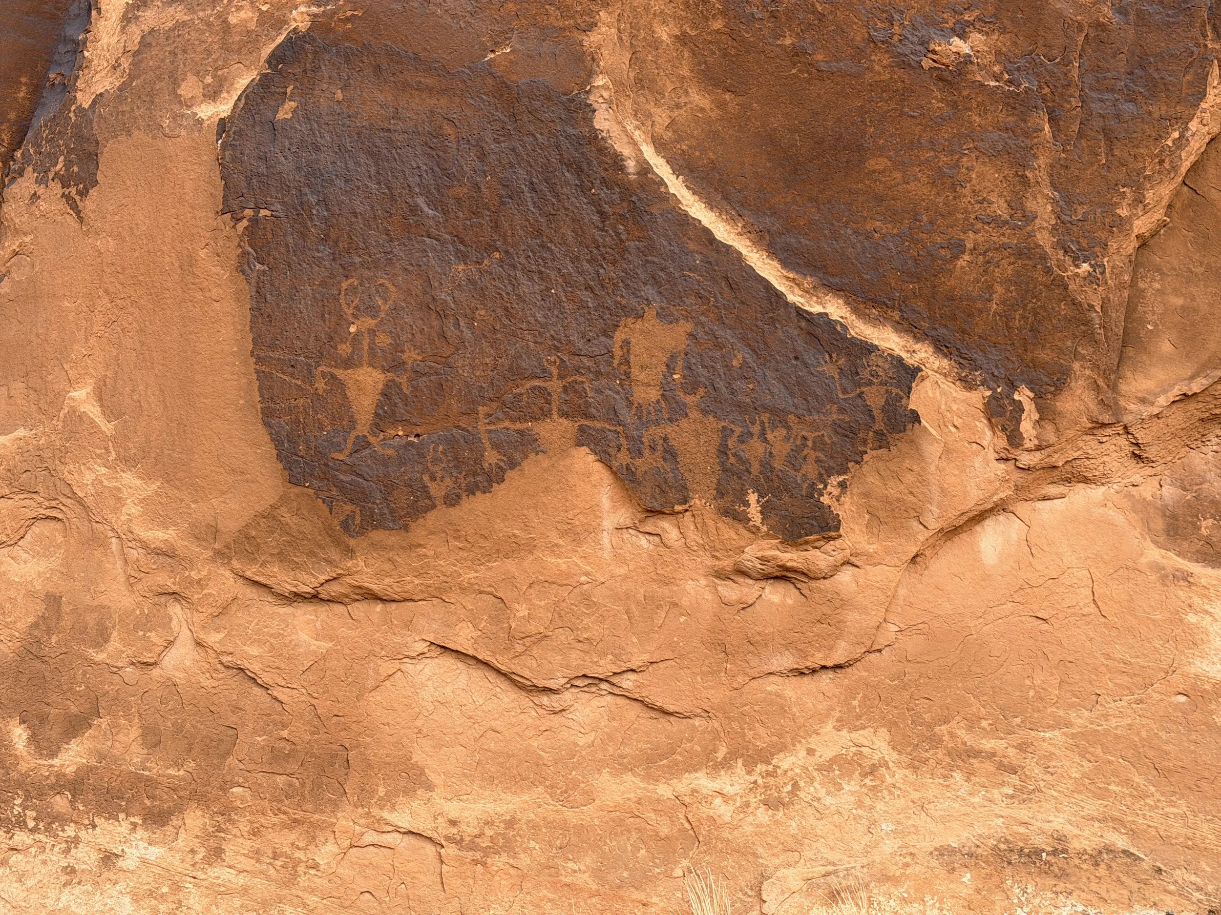 Close-up of Fremont petroglyphs at the Moab Golf Course rock art site near Moab, Utah, showing figures carved through dark desert varnish into lighter sandstone.