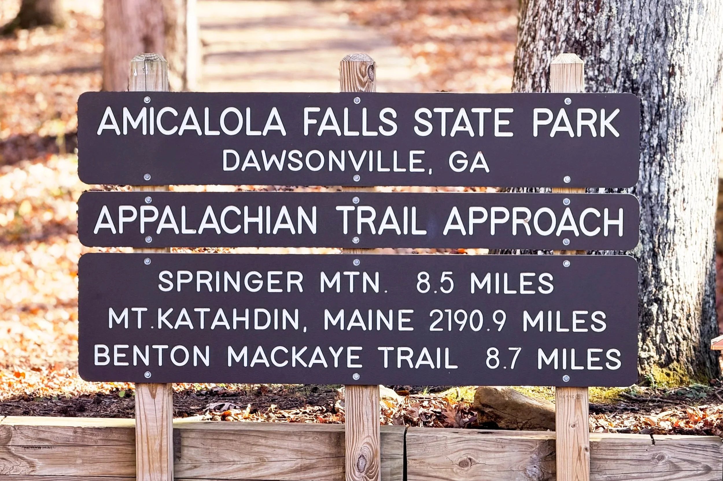Brown wooden sign at Amicalola Falls State Park showing distances to Springer Mountain, Mount Katahdin, and the Benton MacKaye Trail.