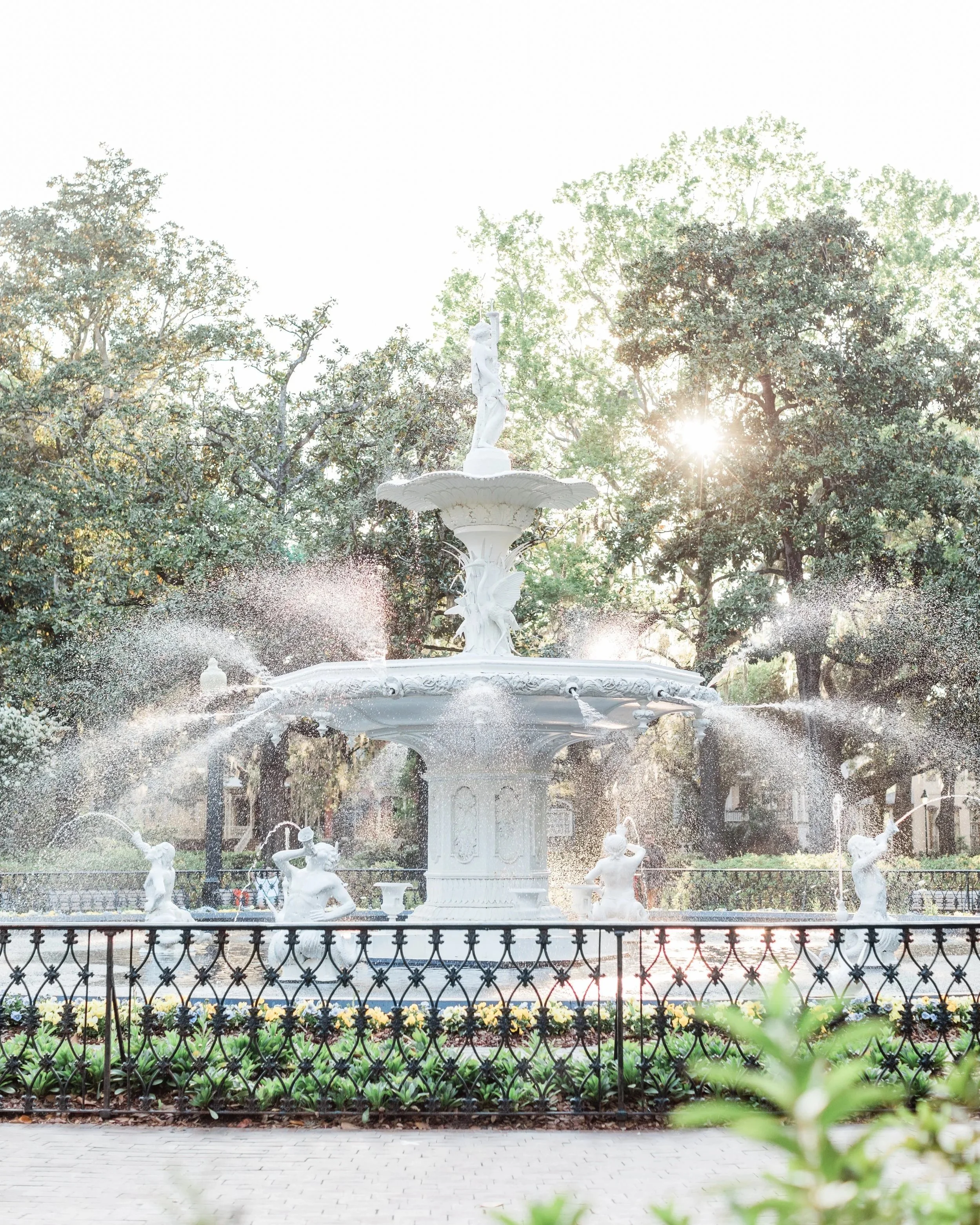 stunning image of the forsyth park fountain in savannah georgia, light shining through the trees and fountain water, greenery and flowers.