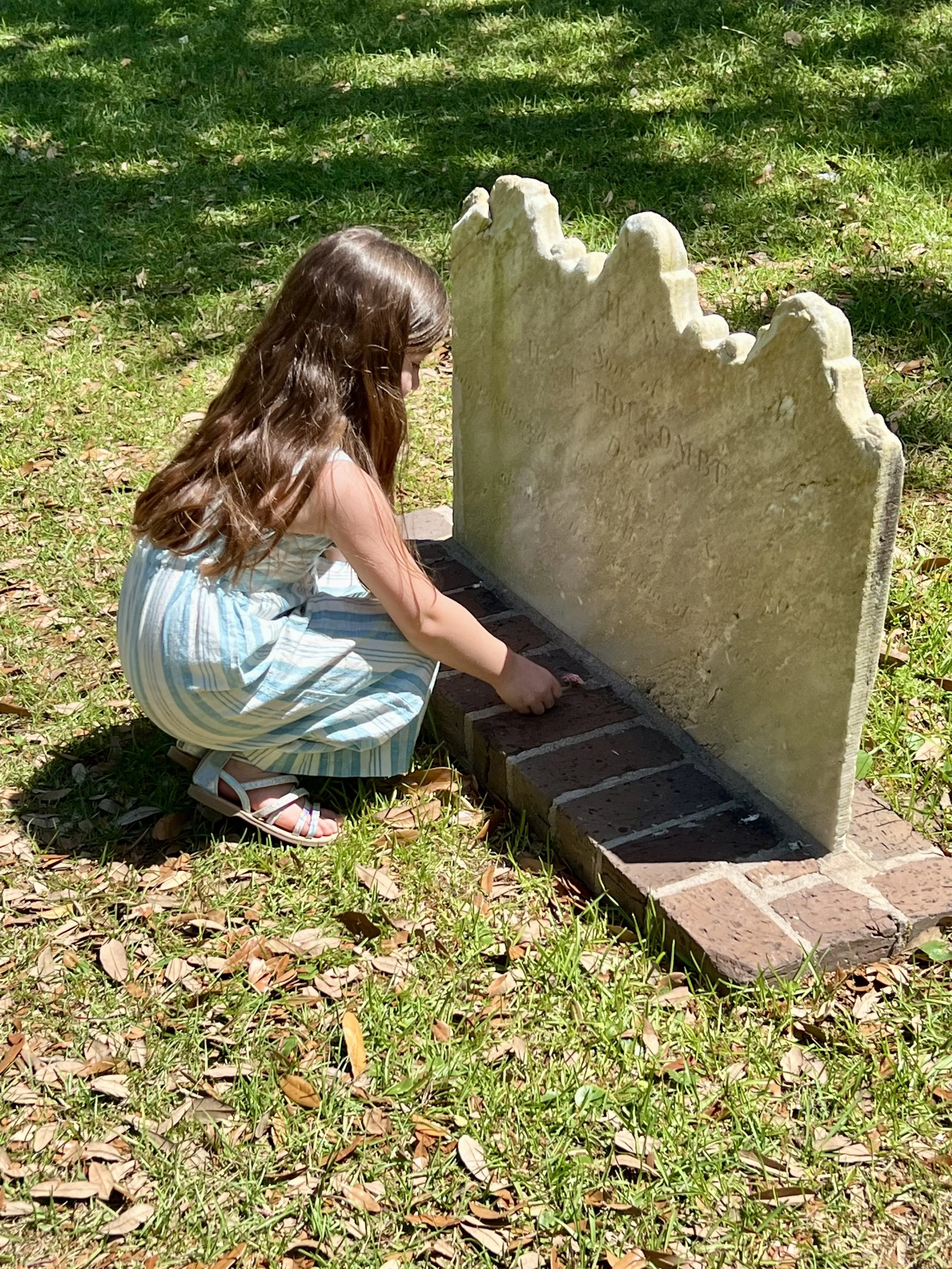 Child placing a coin on a historic gravestone at Bonaventure Cemetery in Savannah, Georgia, reflecting on the city's rich history and peaceful cemetery grounds.